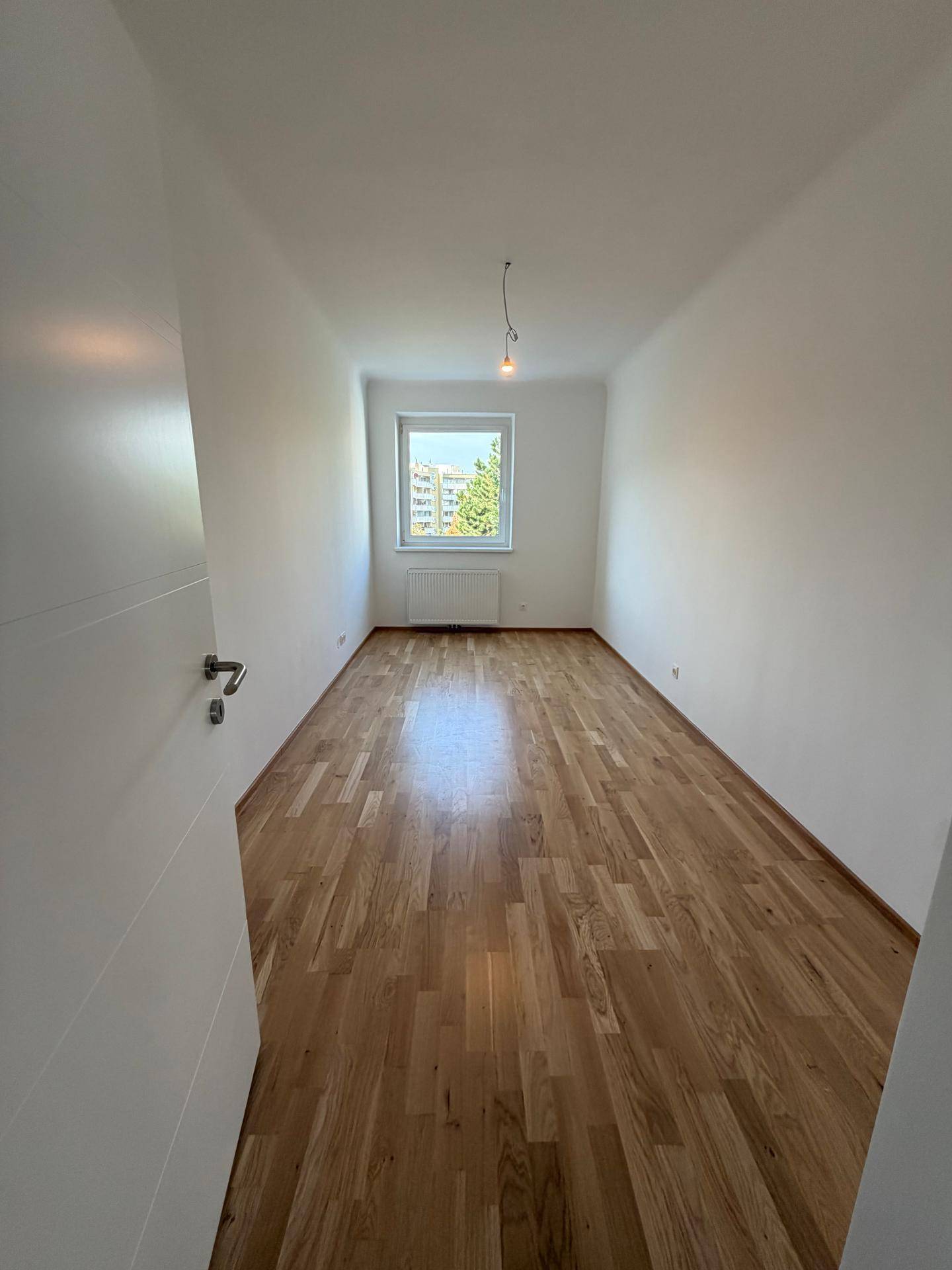 Helles, leeres Zimmer mit Parkettboden und Fenster, ideal als Schlaf- oder Arbeitszimmer nutzbar.