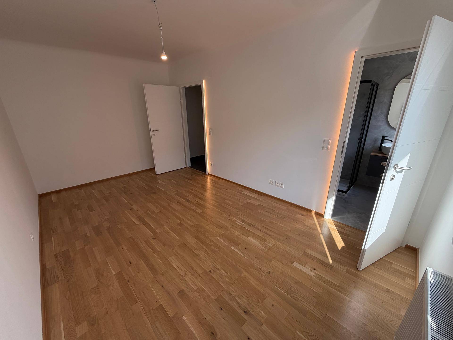Geräumiges Schlafzimmer mit hellem Parkettboden und Zugang zu einem modernen Badezimmer.