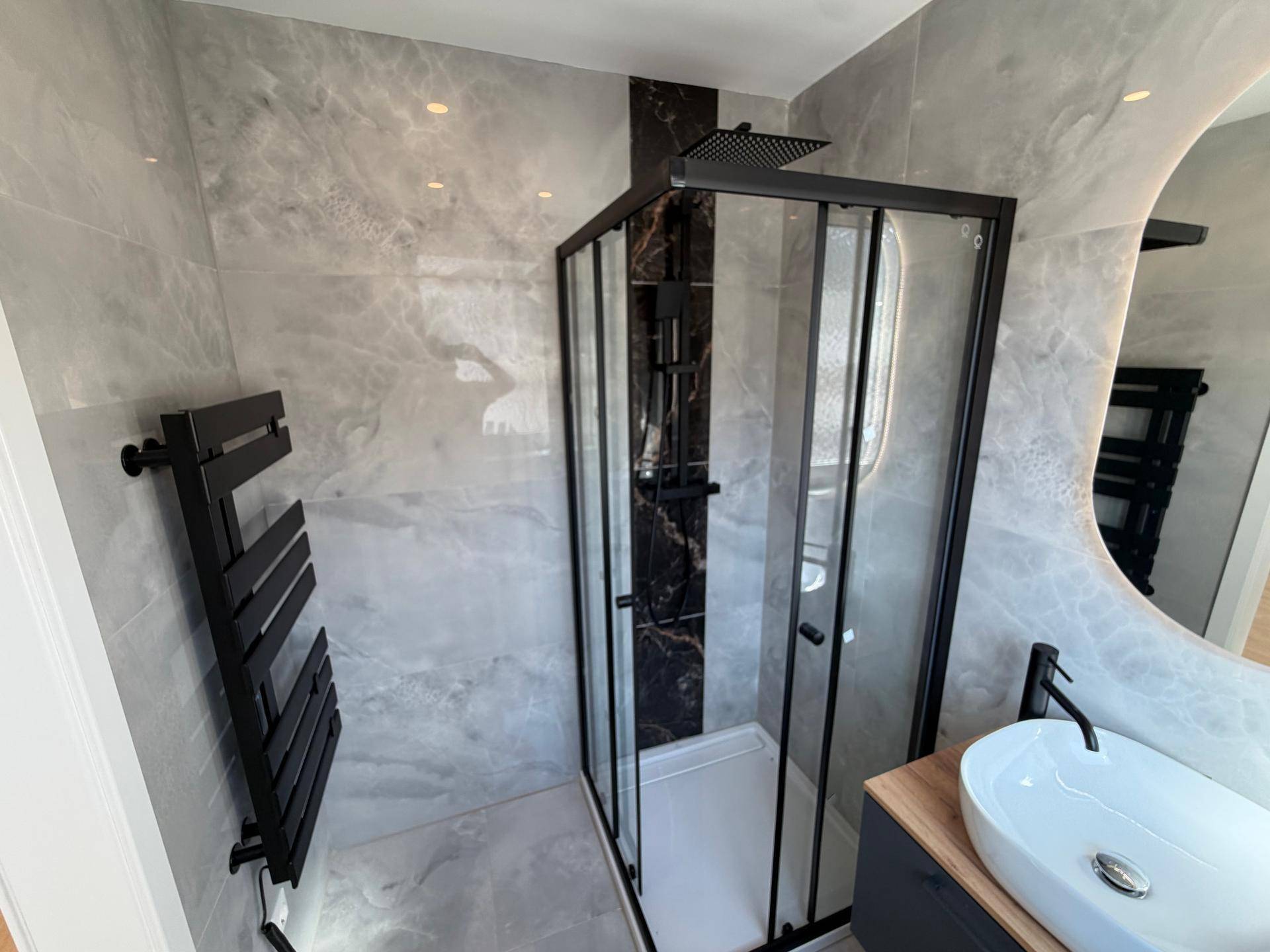 Elegantes Badezimmer mit Duschkabine, ovalem Spiegel, Waschbecken und beheiztem Handtuchhalter.