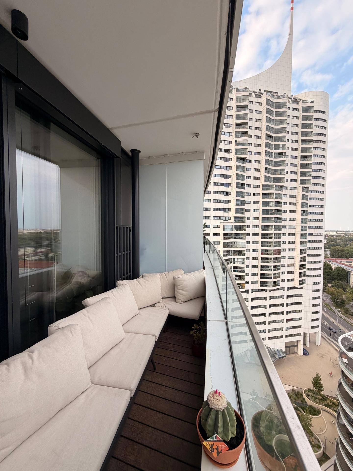 Möblierter Balkon mit bequemer Sitzgruppe und Blick auf ein markantes Hochhaus.