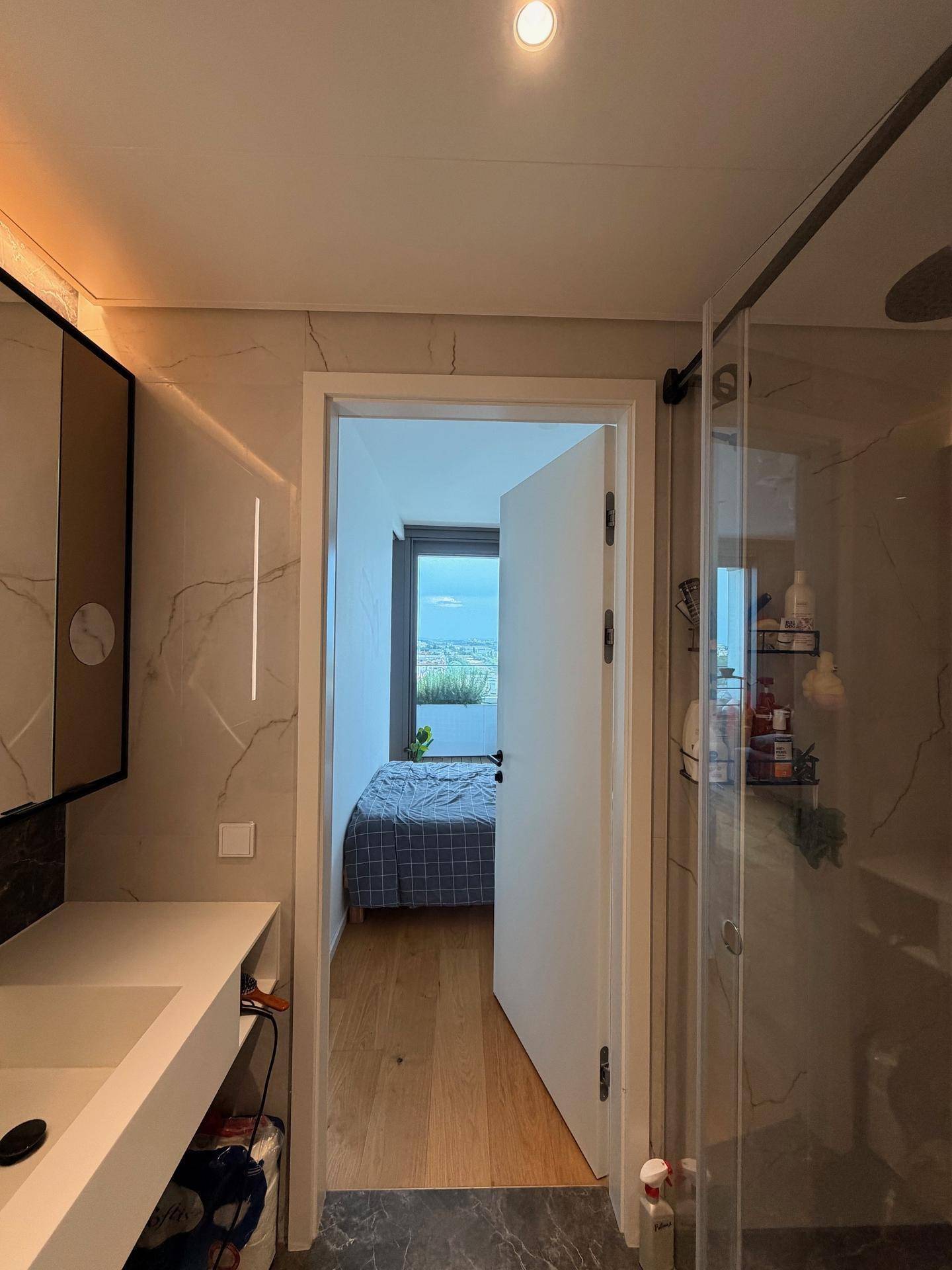 Modernes Badezimmer mit Blick in ein Schlafzimmer, ausgestattet mit Dusche und Waschbecken.