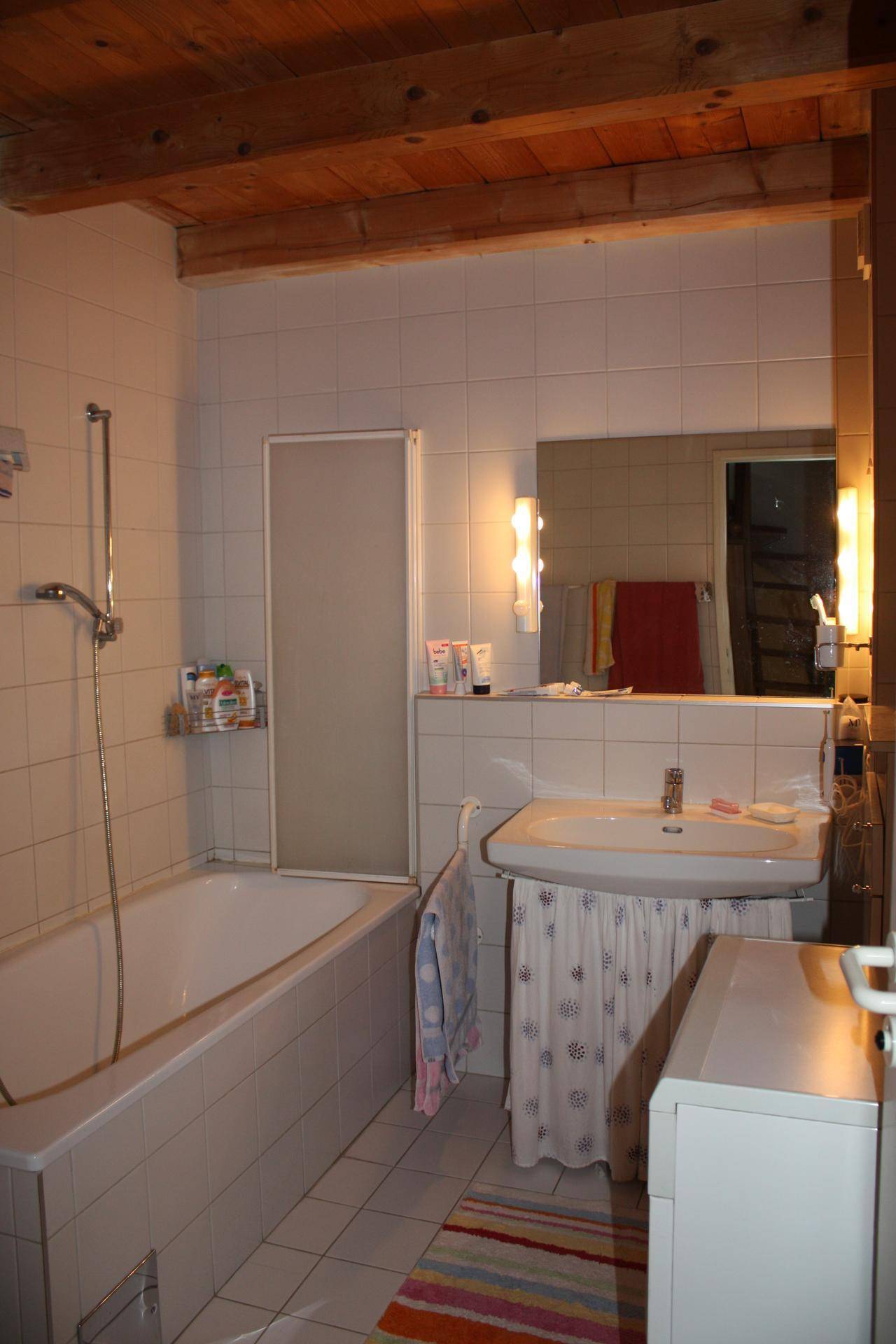 Badezimmer mit Badewanne, Dusche, Waschbecken und sichtbaren Holzdeckenbalken.