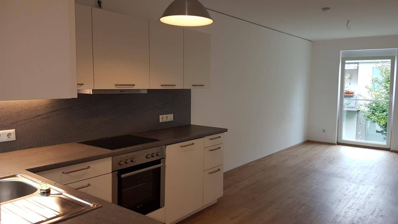 Helle, moderne Küche mit weißen Schränken, dunkler Arbeitsplatte und Zugang zum Balkon.