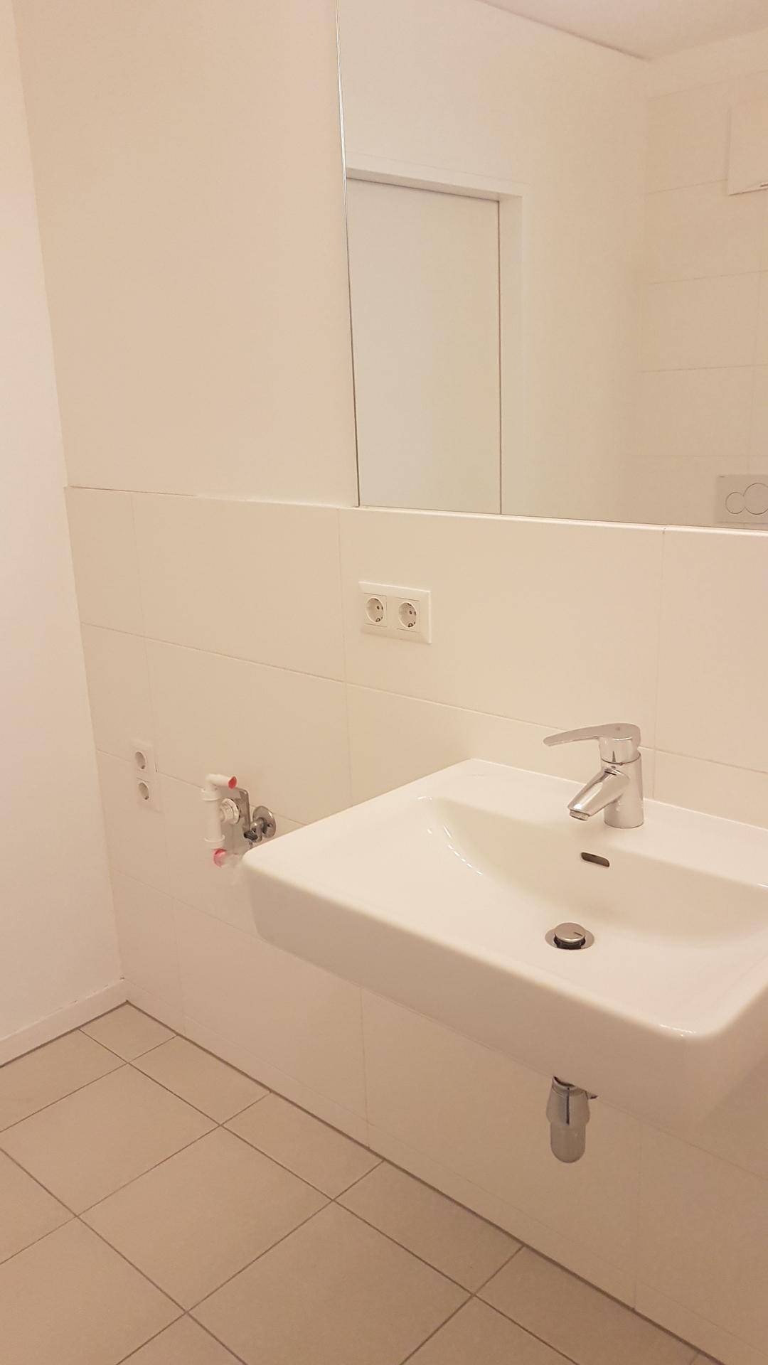 Helles Badezimmer mit modernem Waschbecken, Spiegel und weißen Wandfliesen.