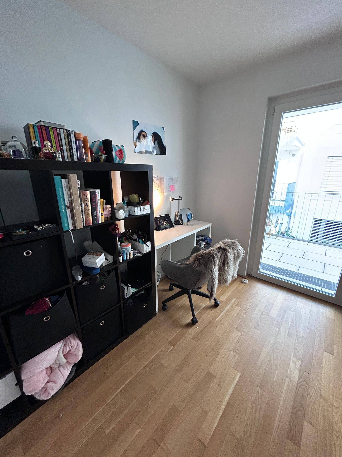 Arbeitsbereich im Schlafzimmer mit Schreibtisch, Regal und Zugang zu einem kleinen Balkon.