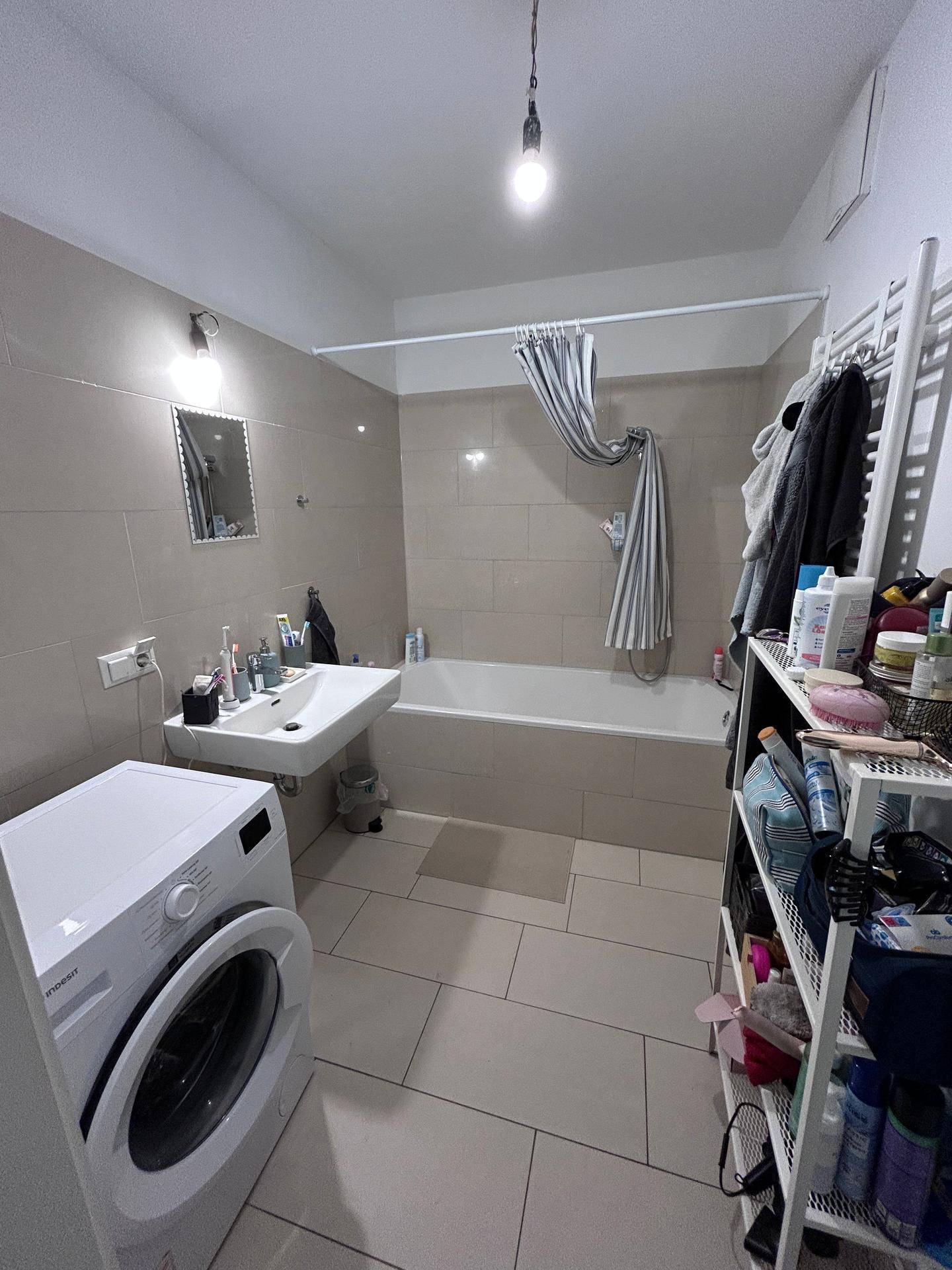 Badezimmer mit Badewanne, Waschbecken, Waschmaschine und hellen Wand- und Bodenfliesen.