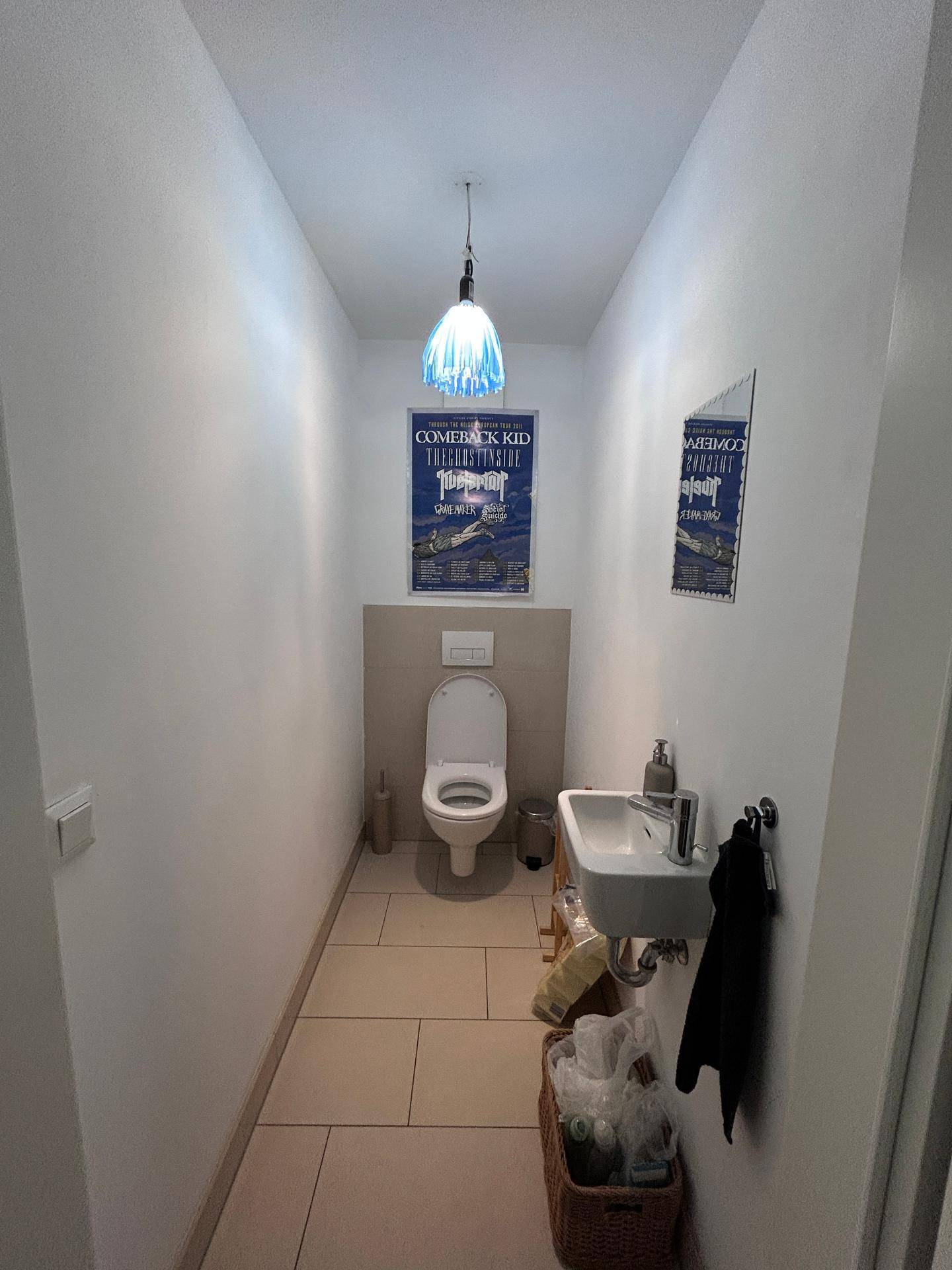 Kleines Gäste-WC mit Toilette, Waschbecken und hellen Fliesen auf dem Boden.