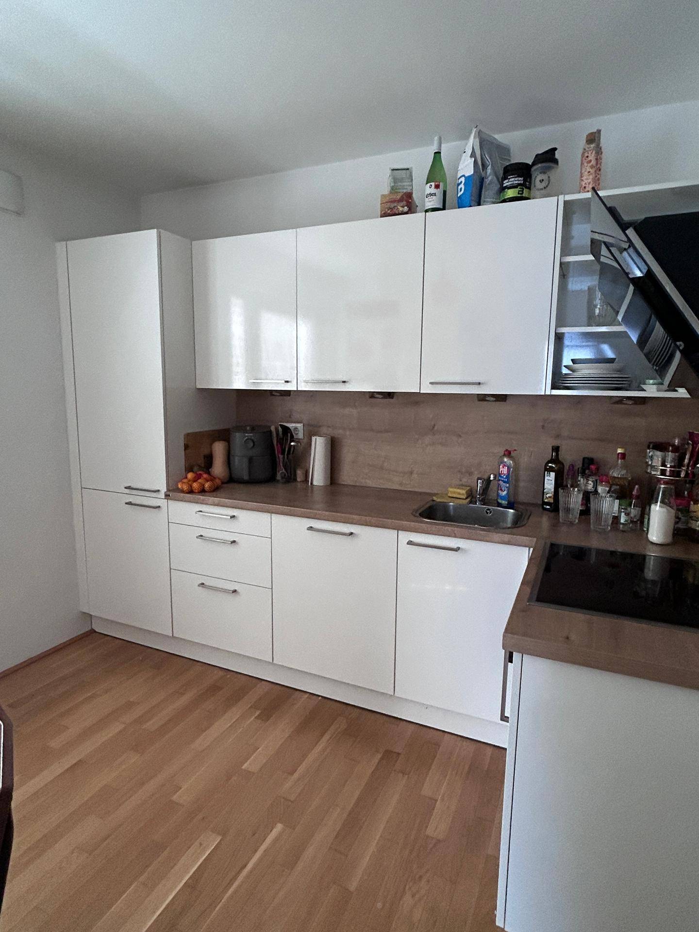 Moderne Küche mit weißen Hochglanzschränken, Holzarbeitsplatte und Induktionskochfeld.