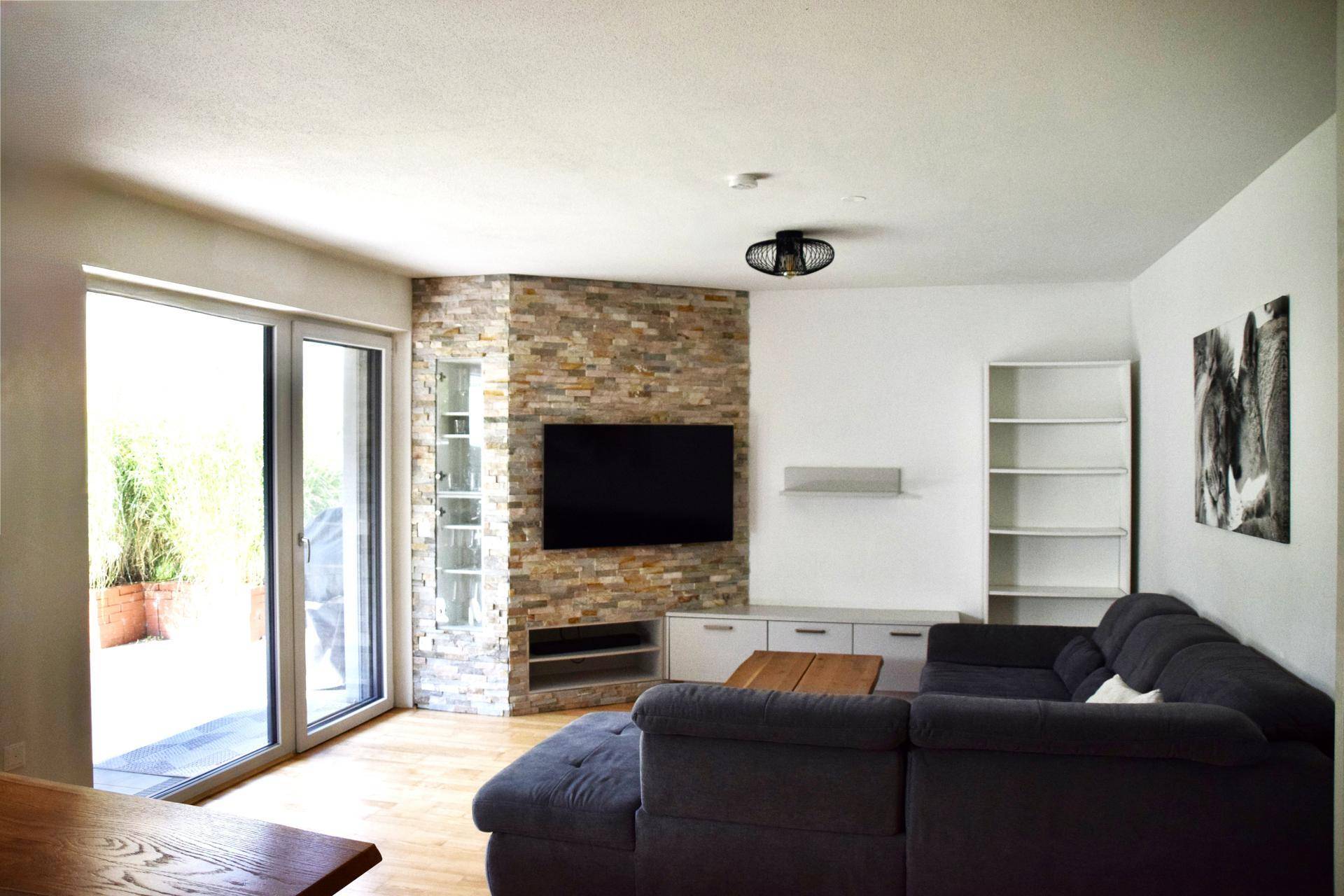 Gemütliches Wohnzimmer mit großem Sofa, Steinwand und Zugang zur Terrasse oder Garten.