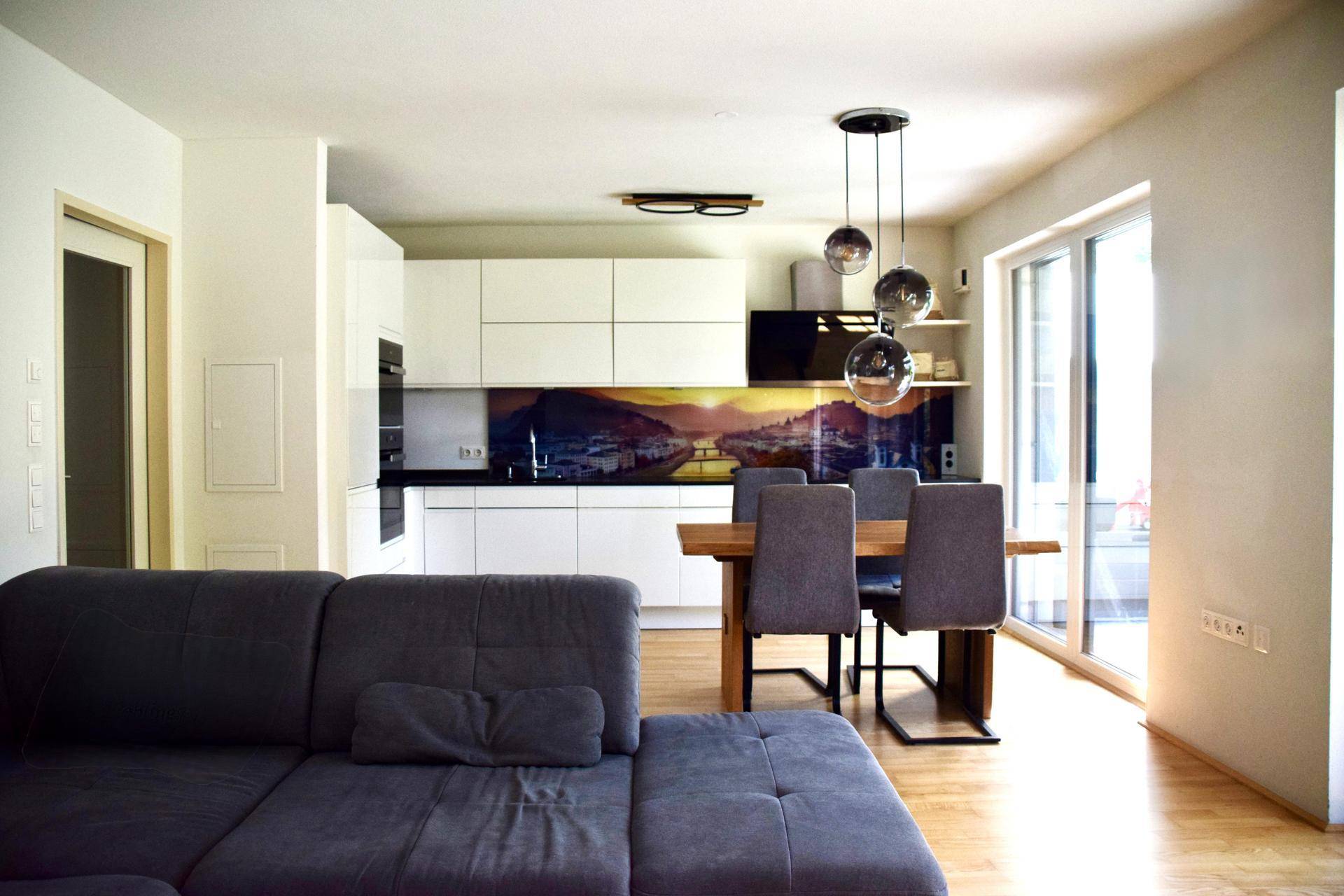 Offener Wohnbereich mit bequemer Couch, Esstisch und moderner Küche im Hintergrund.