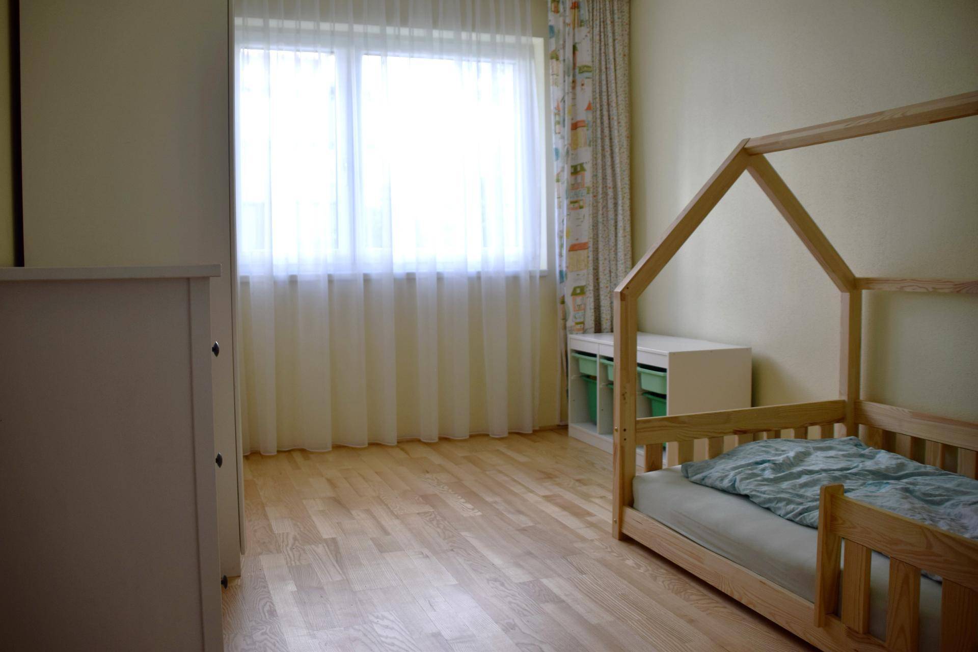 Kinderzimmer mit hellem Holzbett, freundlichen Vorhängen und viel Tageslicht.