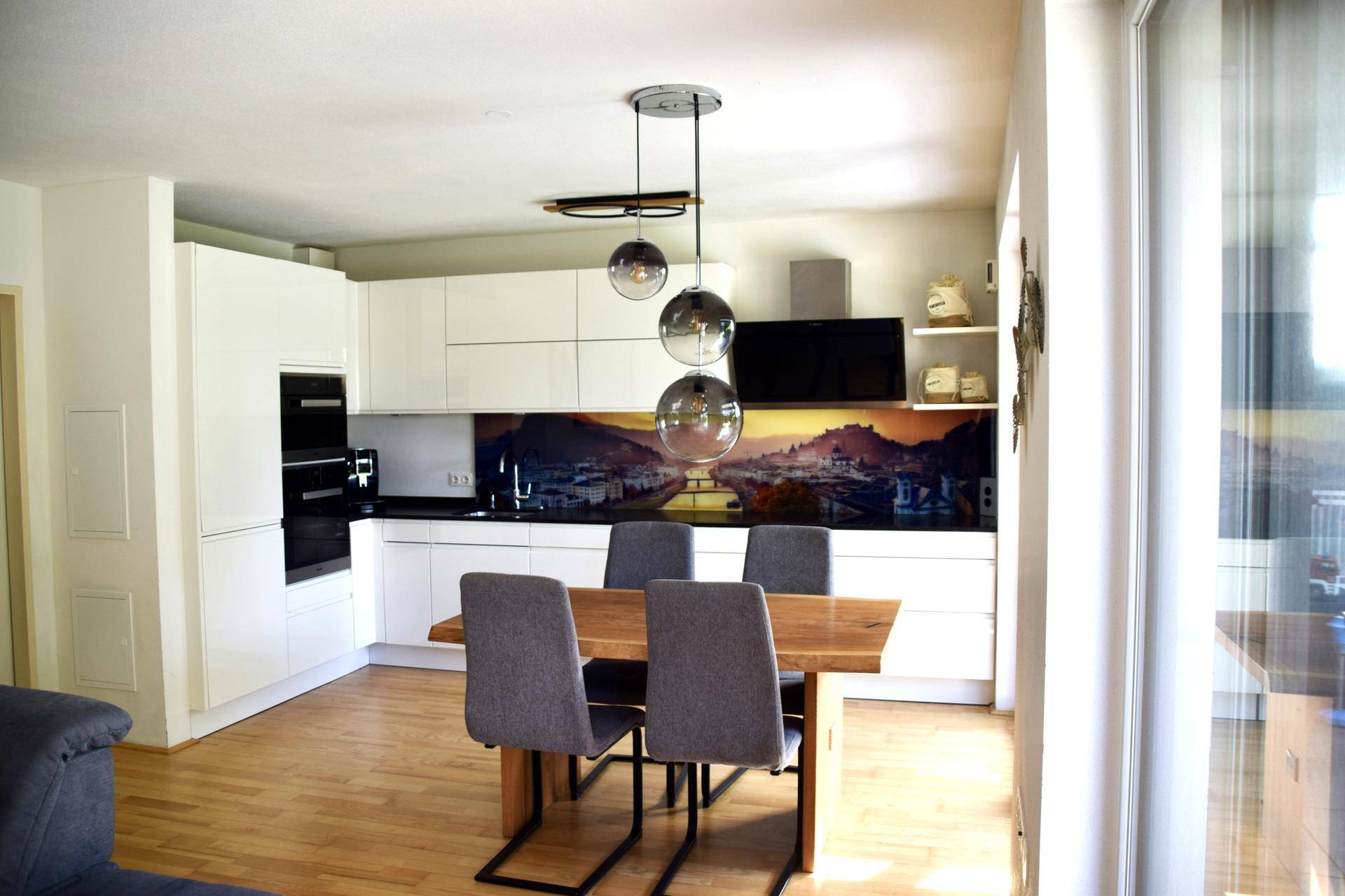 Moderne weiße Küche mit integrierten Geräten, Holztisch und dekorativer Rückwand.