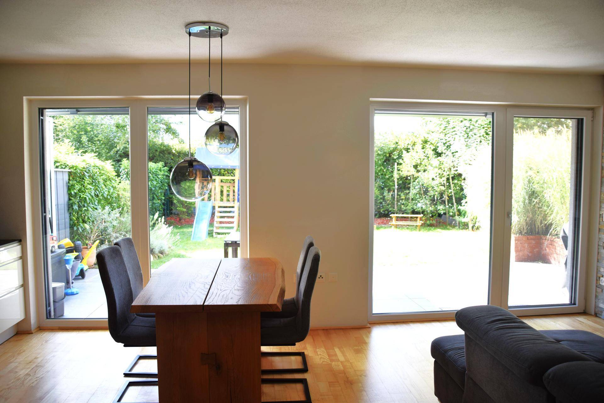 Heller Wohn- und Essbereich mit Holztisch und Blick auf den grünen Garten mit Spielplatz.
