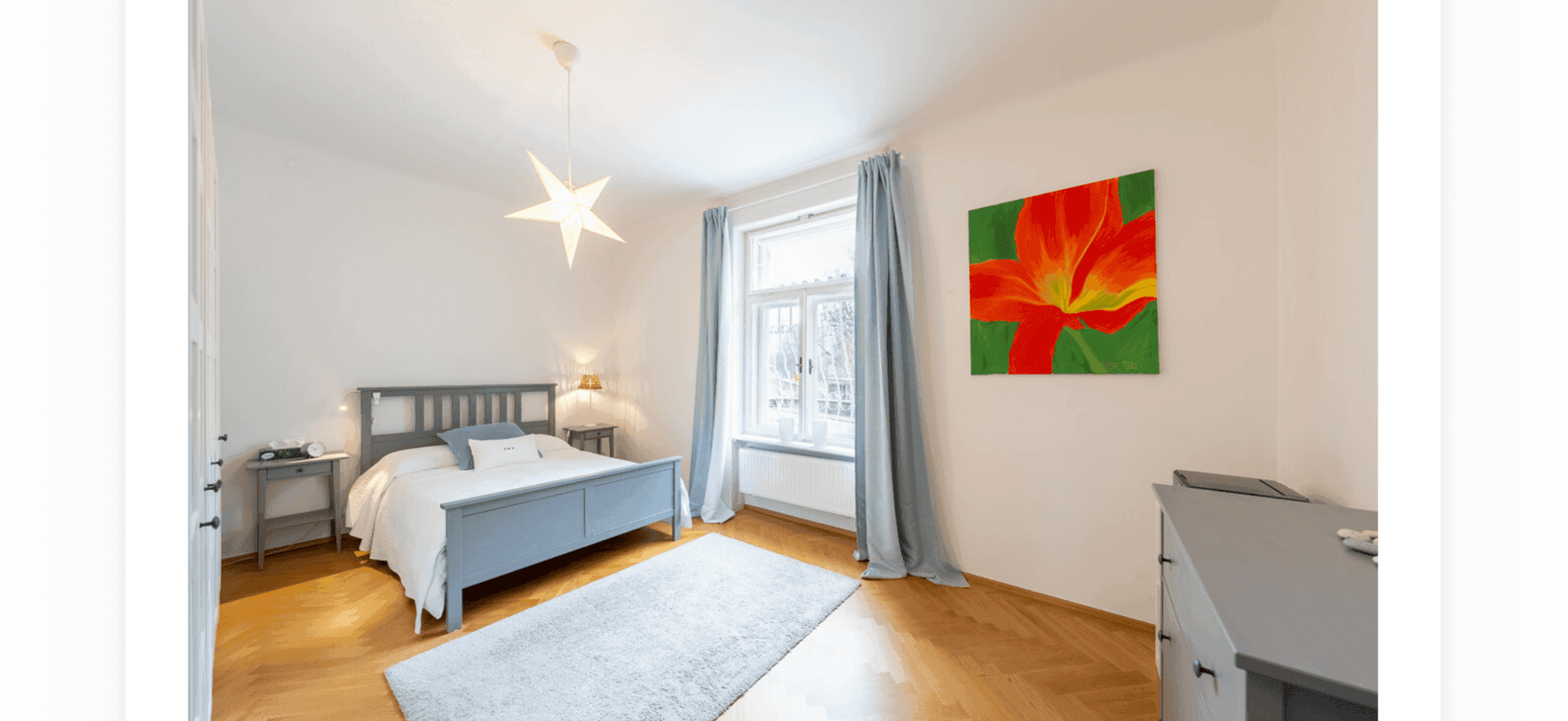 Helles Schlafzimmer mit Doppelbett, Fischgrätparkett und farbenfrohem Kunstwerk.