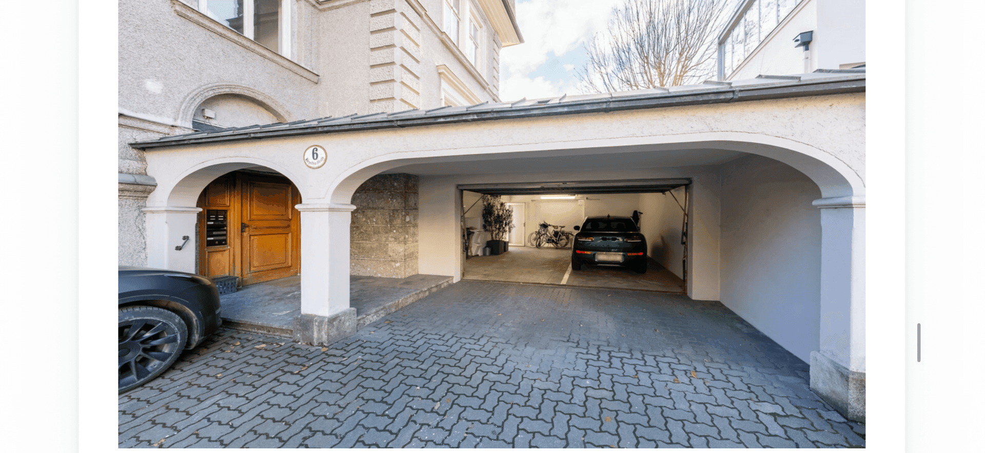 Eingangsbereich mit Holztür und integrierter Garage sowie Carport für Fahrzeuge.