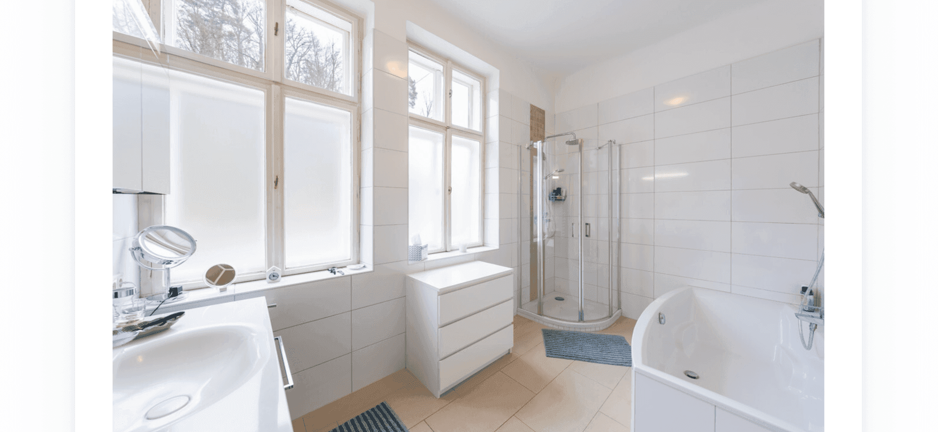 Helles Badezimmer mit Badewanne, Dusche, Fenster und weißen Fliesen.