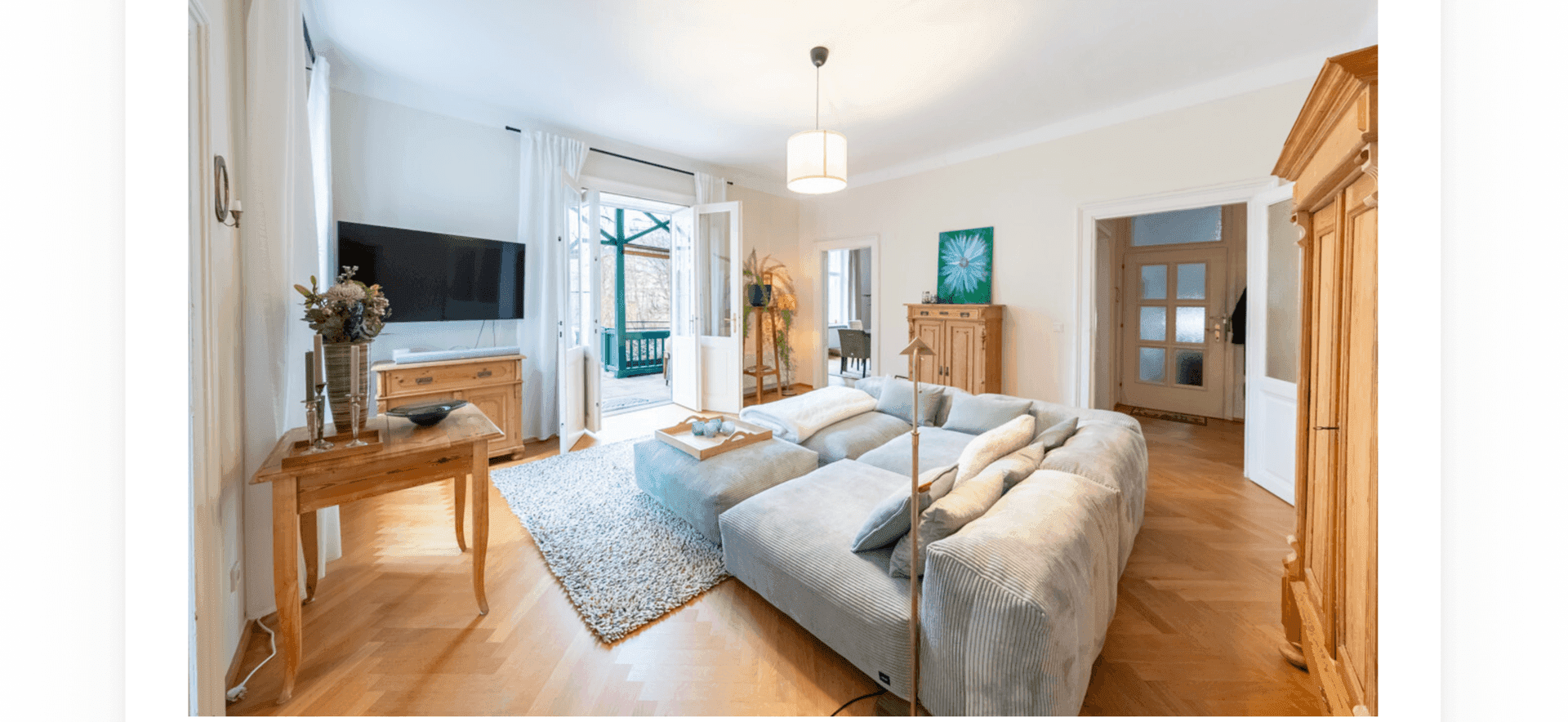 Gemütliches Wohnzimmer mit großem Sofa, Fischgrätparkett und Zugang zum Balkon.