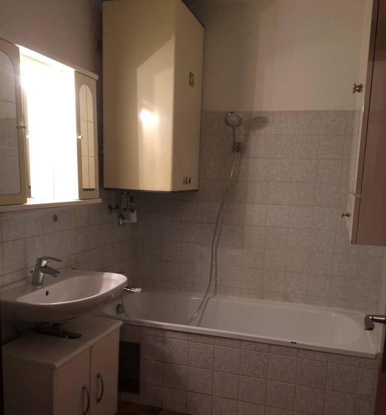 Badezimmer mit Badewanne, Waschbecken, Fenster und Wandfliesen im Stil der 80er Jahre.