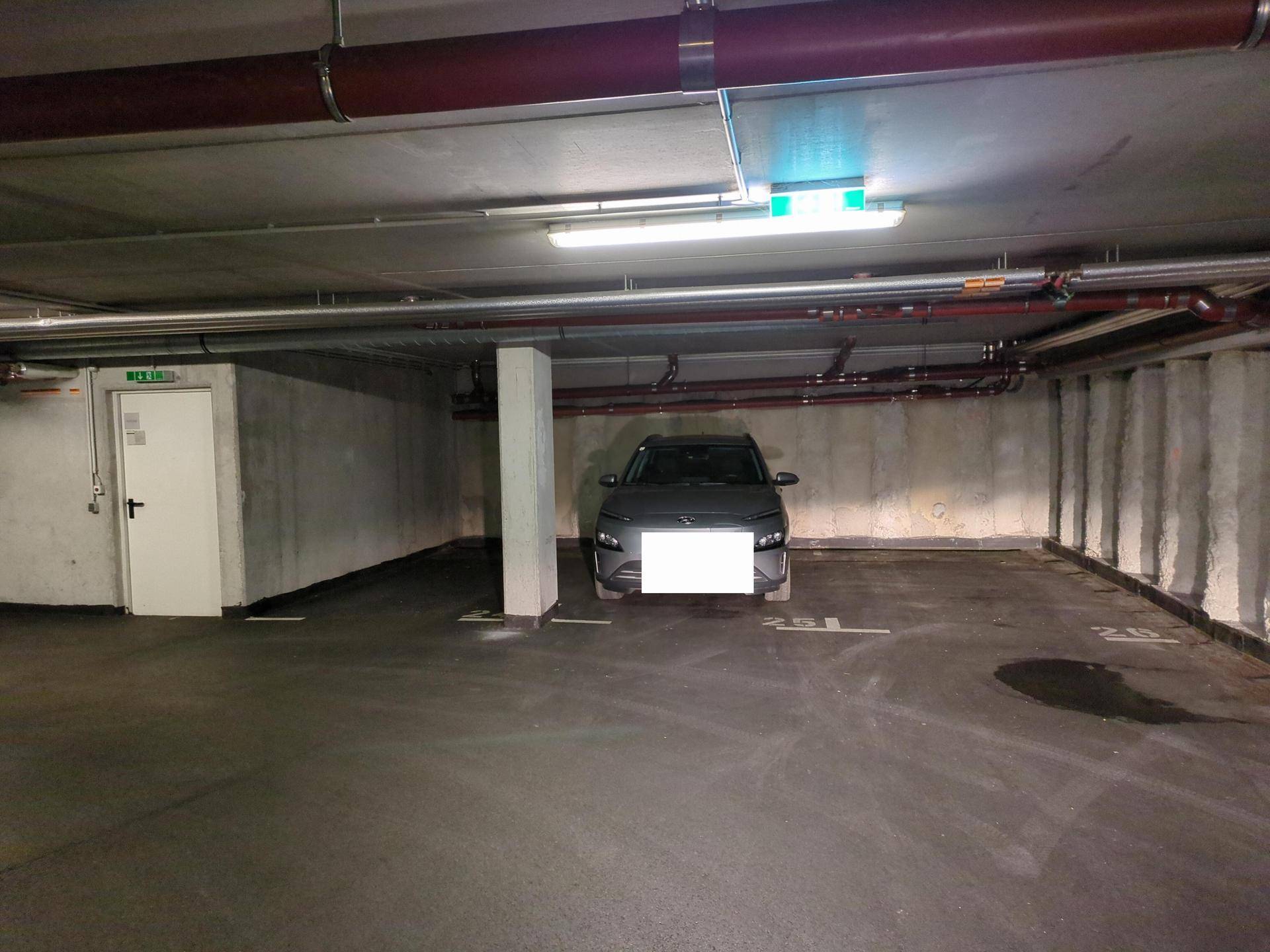 Geräumige Tiefgarage mit mehreren Stellplätzen, Betonstützen und Zugangstür.