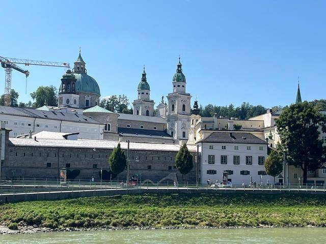 Historische Stadtansicht mit imposanten Gebäuden, einem Fluss im Vordergrund und einem Baukran.