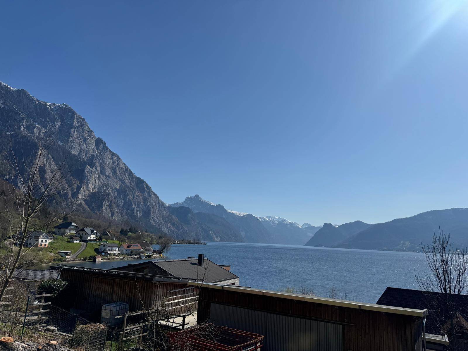 Sonniger Ausblick auf einen blauen See und imposante Berge unter klarem Himmel.
