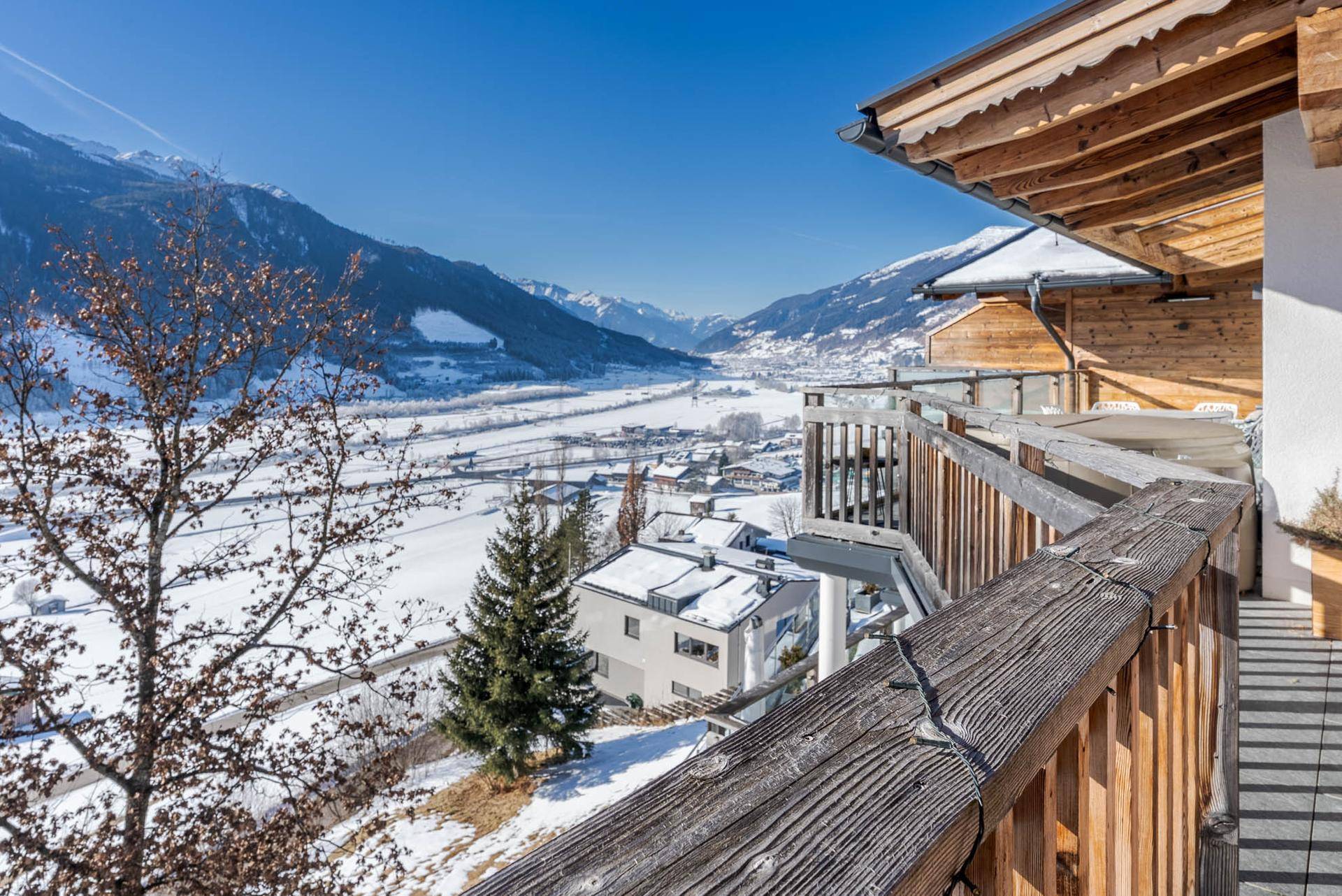 Geräumiger Holzbalkon mit Blick auf das verschneite Tal und die umliegenden Berge.