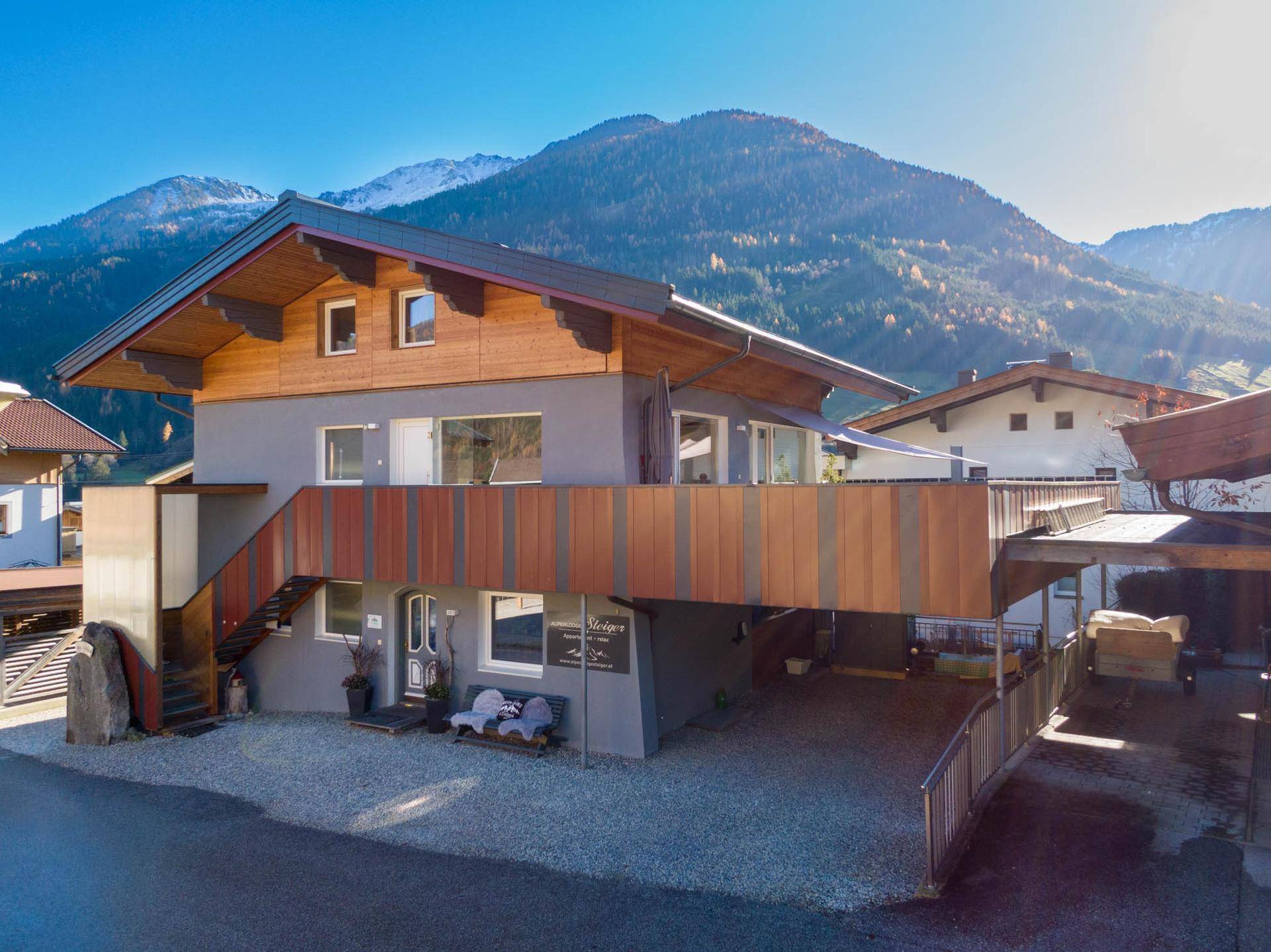 Modernes Haus mit Holzakzenten und großzügiger Terrasse, umgeben von verschneiten Bergen.