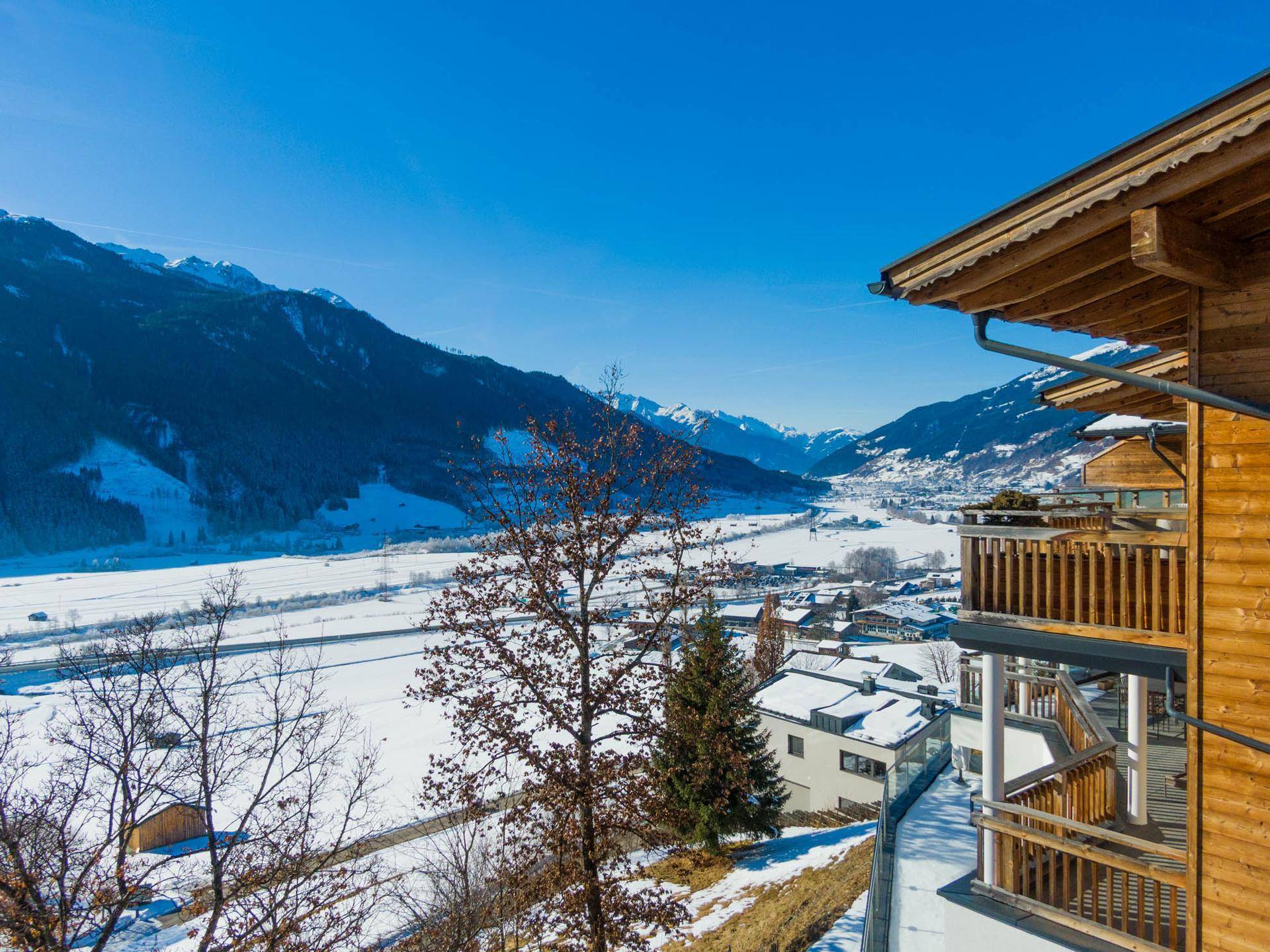 Panoramablick auf das verschneite Tal und die Berge von einem Balkon eines Holzchalets.