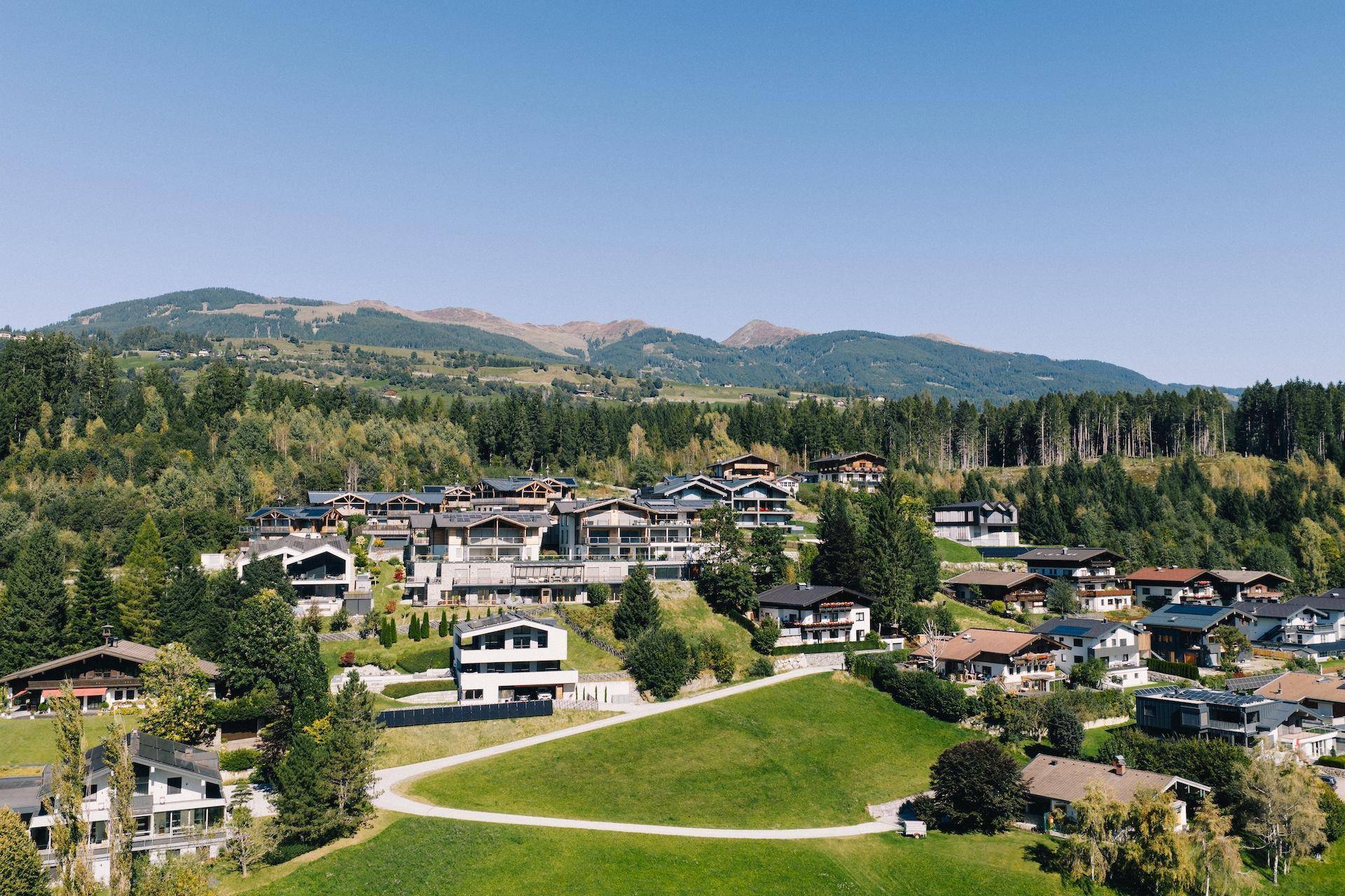 Sommerliche Luftaufnahme einer luxuriösen Wohnanlage in den Bergen mit viel Grün und Wald.