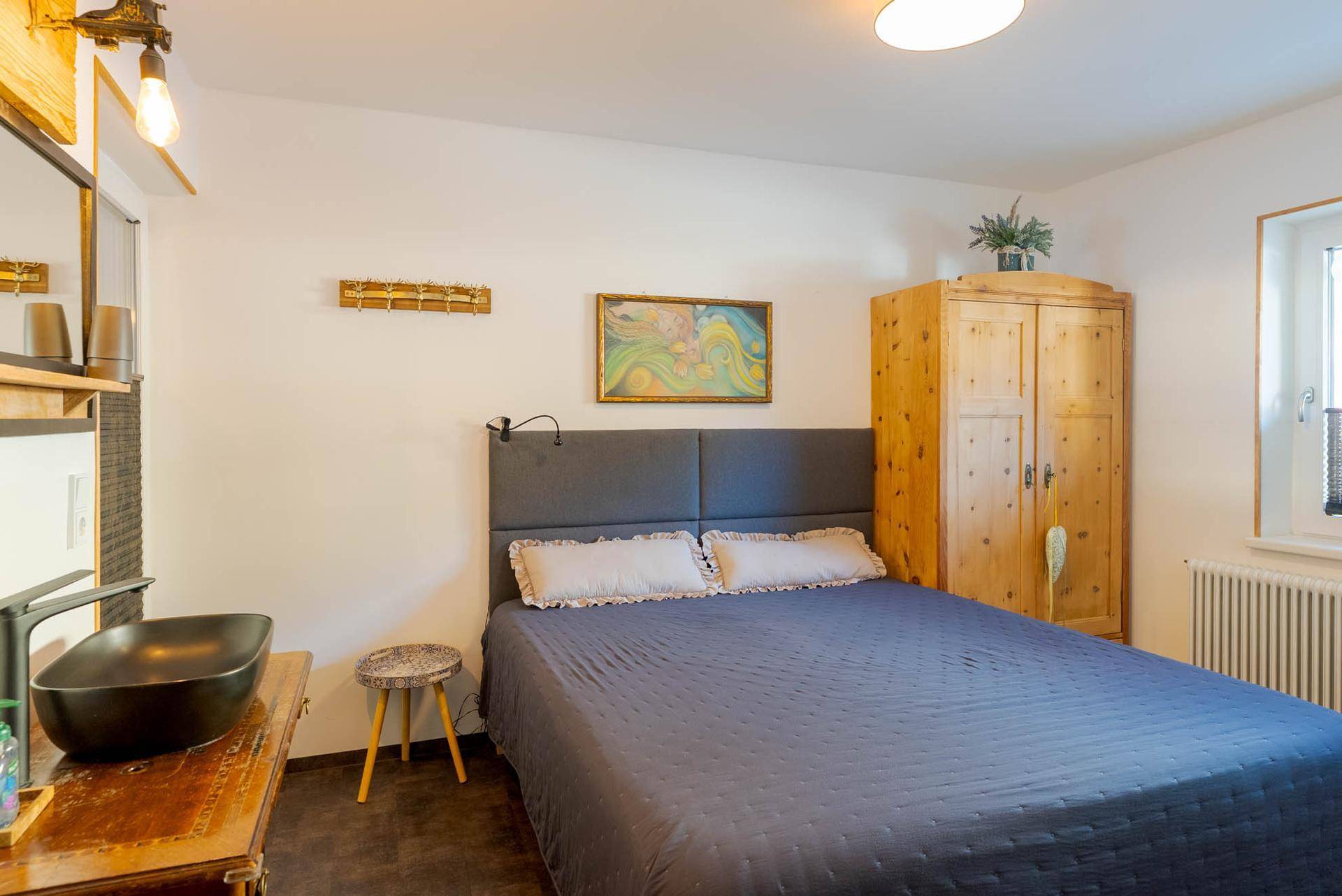 Gemütliches Schlafzimmer mit Doppelbett, Holzkleiderschrank und integriertem Waschbecken.