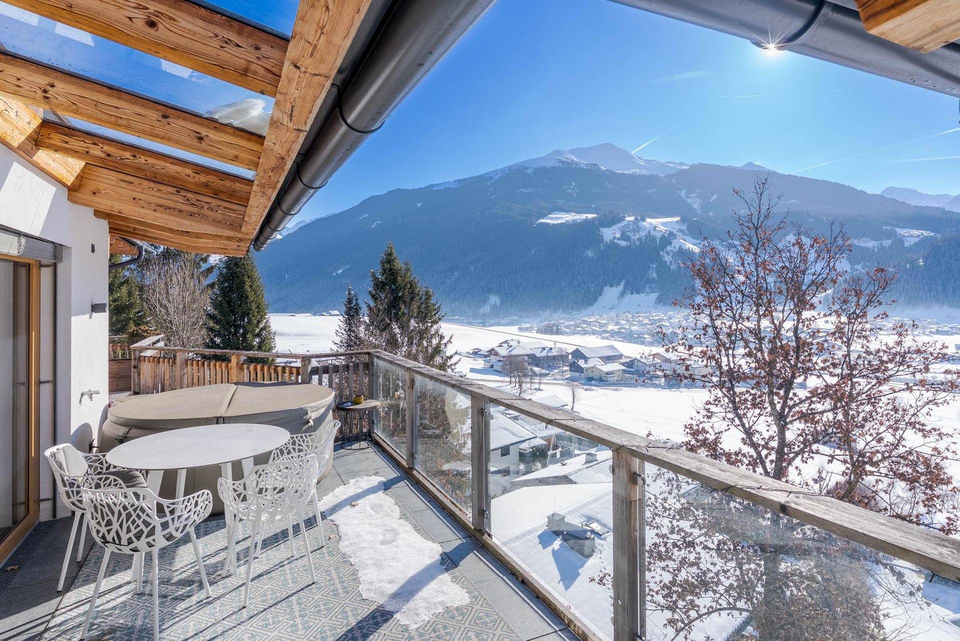 Sonniger Balkon mit Whirlpool, Sitzgelegenheiten und atemberaubendem Bergblick.