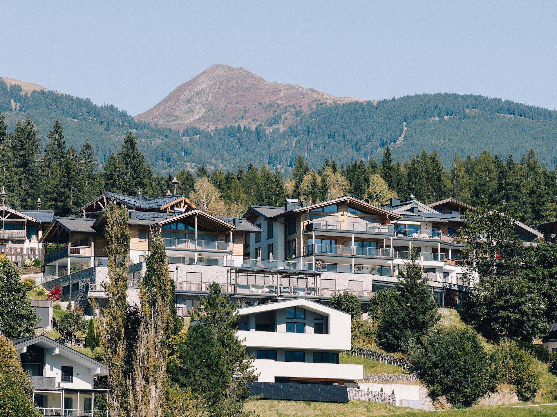 Luxuriöse Wohnanlage in den Bergen mit moderner Architektur, großen Balkonen und grüner Umgebung.