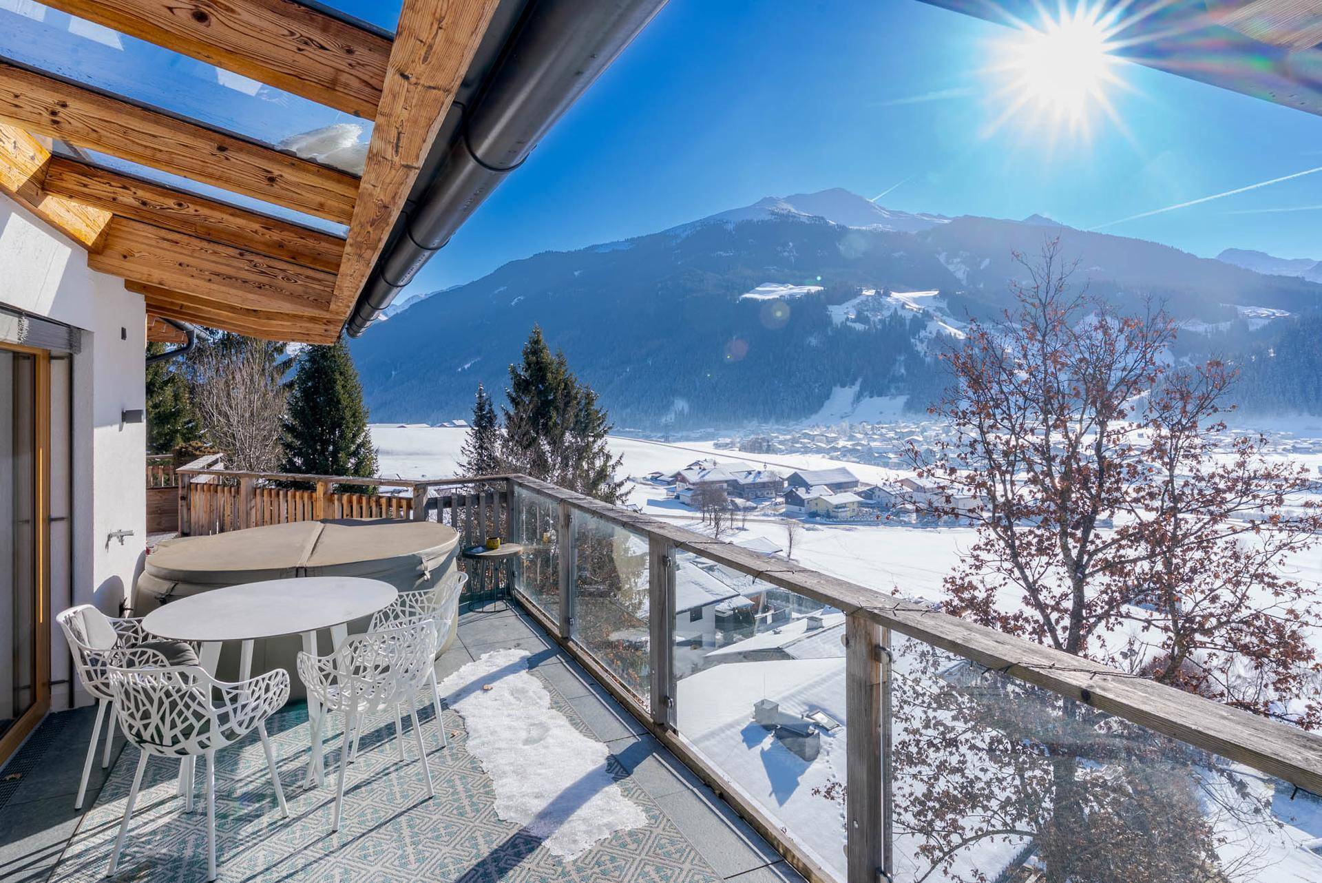 Sonniger Balkon mit Whirlpool, Sitzgelegenheiten und atemberaubendem Bergblick.