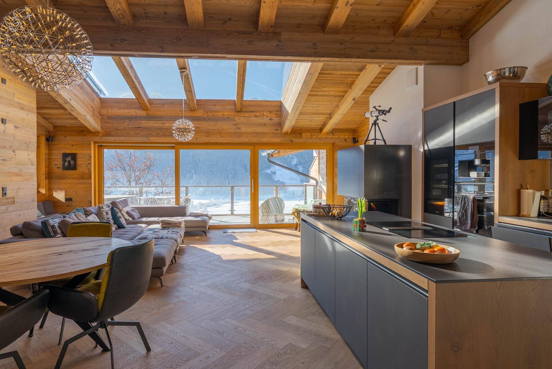 Offener Wohn-Essbereich mit moderner Küche, Holzbalken und Zugang zum Balkon.