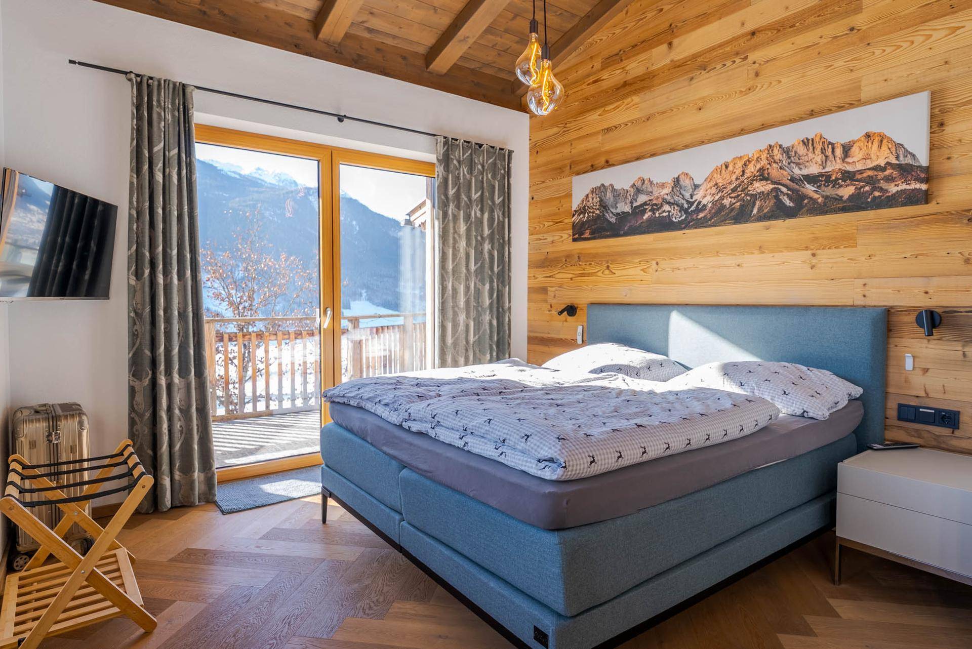 Gemütliches Schlafzimmer mit Holzwänden, Doppelbett und Balkonzugang mit Bergblick.