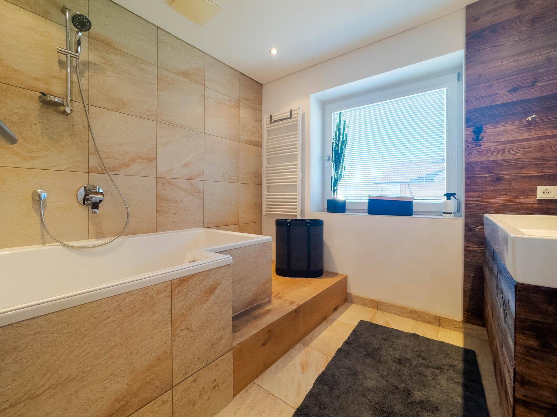 Geräumiges Badezimmer mit Badewanne, Dusche, Holzdetails und Fenster für Tageslicht.