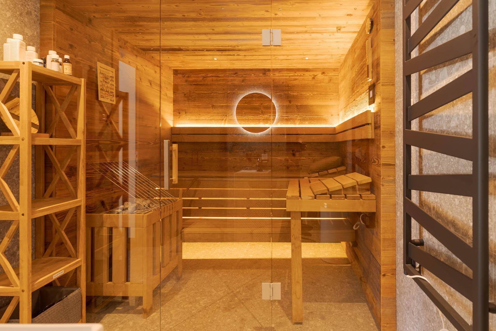 Moderne Sauna mit Holzbänken, Glasfront und indirekter Beleuchtung im Wellnessbereich.