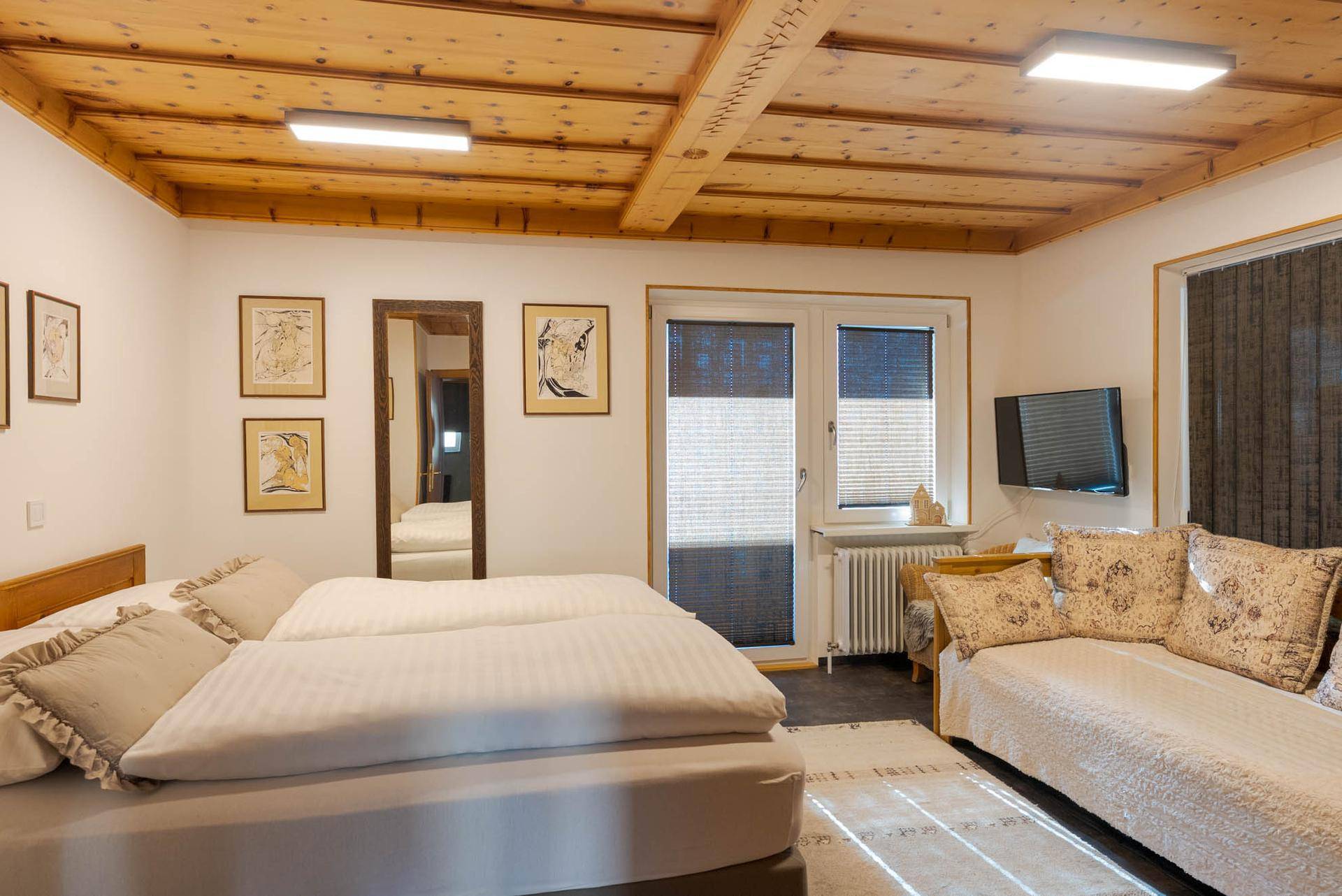 Helles Schlafzimmer mit zwei Einzelbetten, Holzbalkendecke und Zugang zum Balkon.