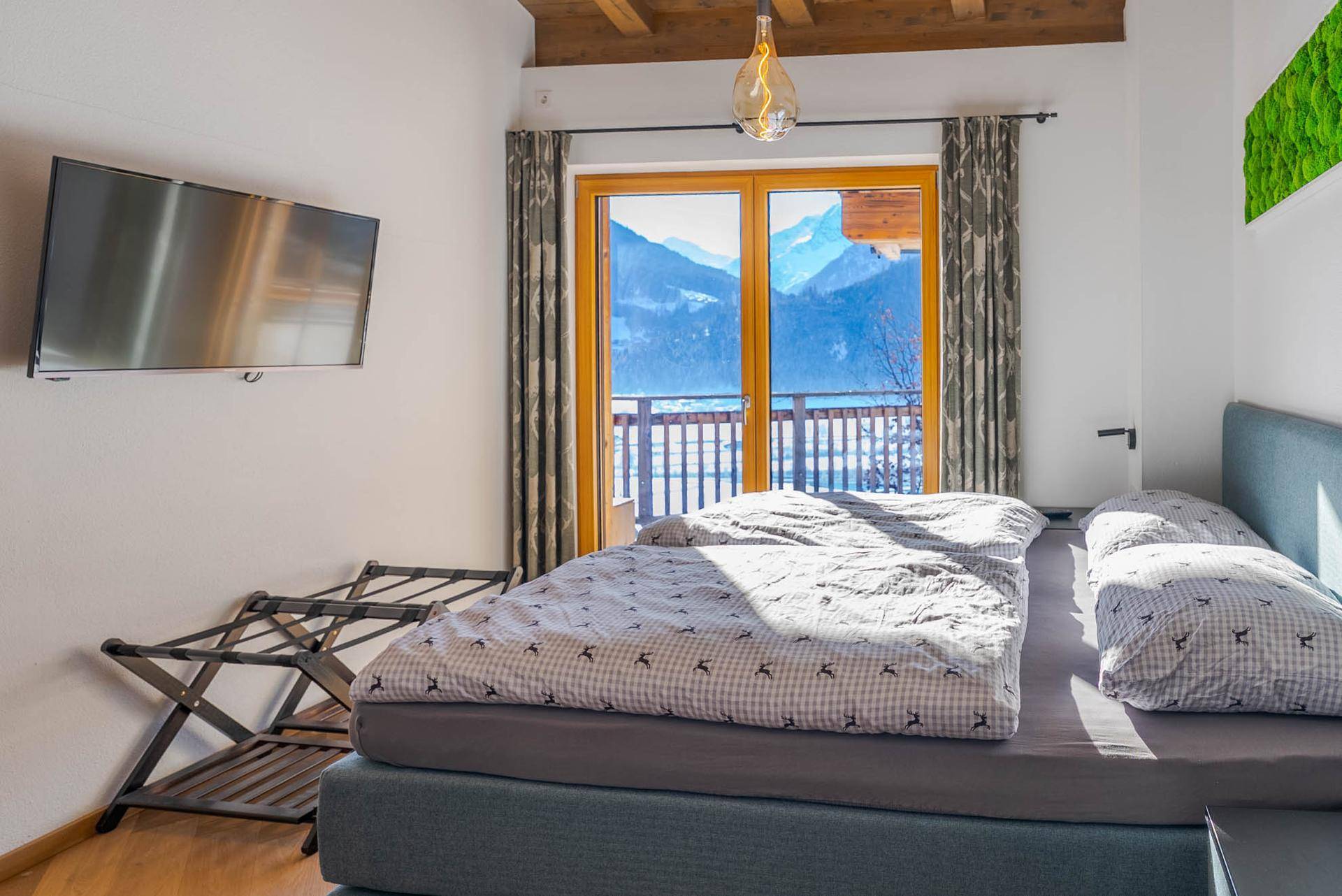 Gemütliches Schlafzimmer mit Doppelbett, Holzboden und Balkonzugang mit Bergblick.