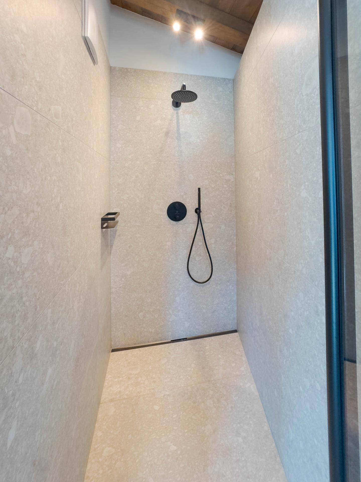 Moderne begehbare Dusche mit dunklen Armaturen und großformatigen hellgrauen Fliesen.