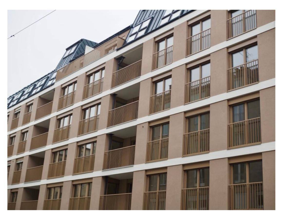 Moderne Wohnhausfassade mit zahlreichen Balkonen und großen Fenstern unter einem Mansarddach.