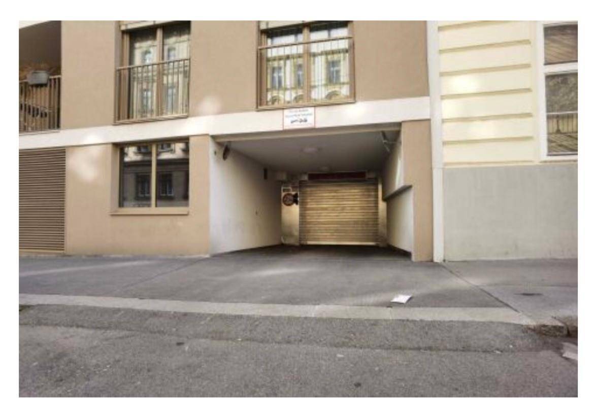 Einfahrt zu einer Tiefgarage von der Straße aus, umgeben von einer modernen Gebäudefassade.