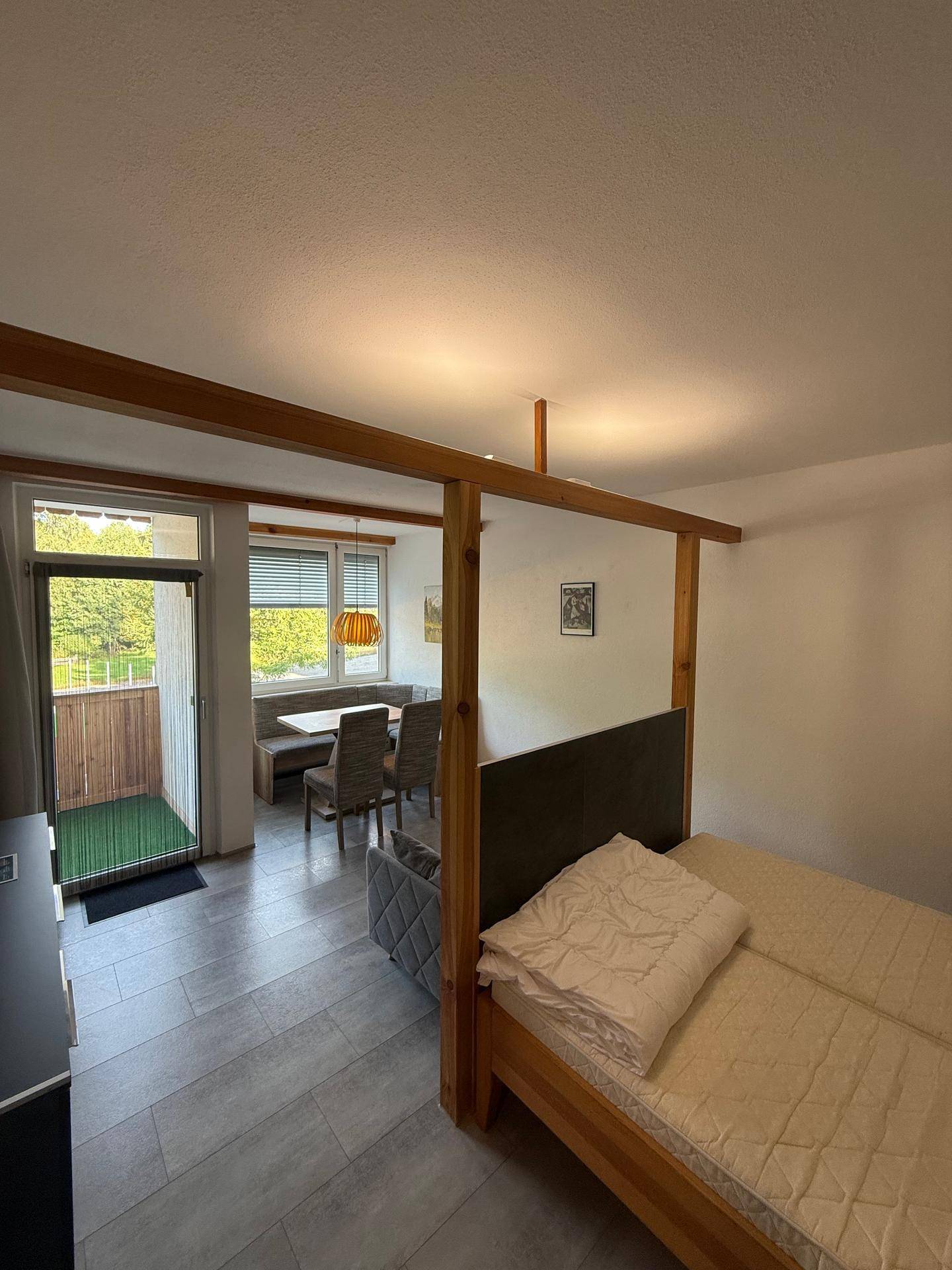 Kombinierter Wohn- und Essbereich mit Bett, Esstisch und Zugang zum Balkon.