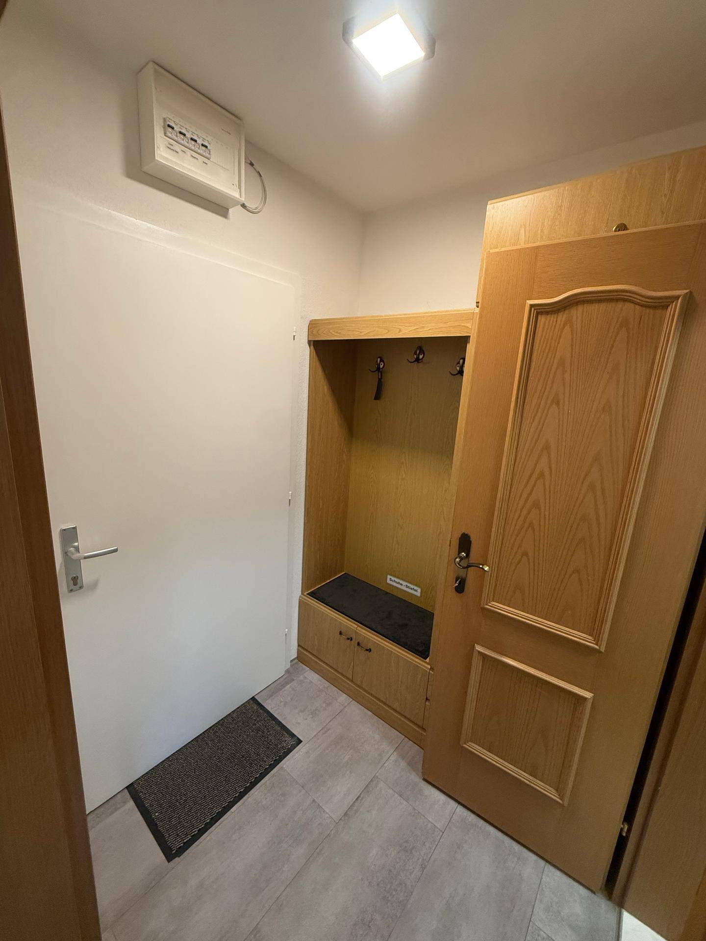 Eingangsbereich mit integrierter Garderobe, Holztüren und grauen Bodenfliesen.