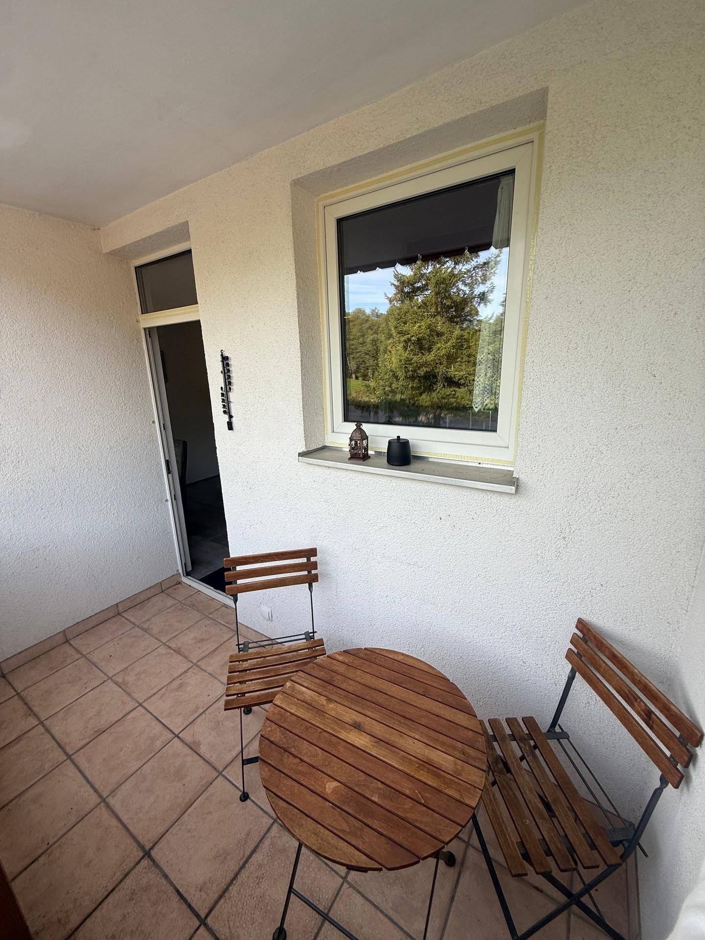 Balkon mit Holztisch und Stühlen, umgeben von weißer Fassade.