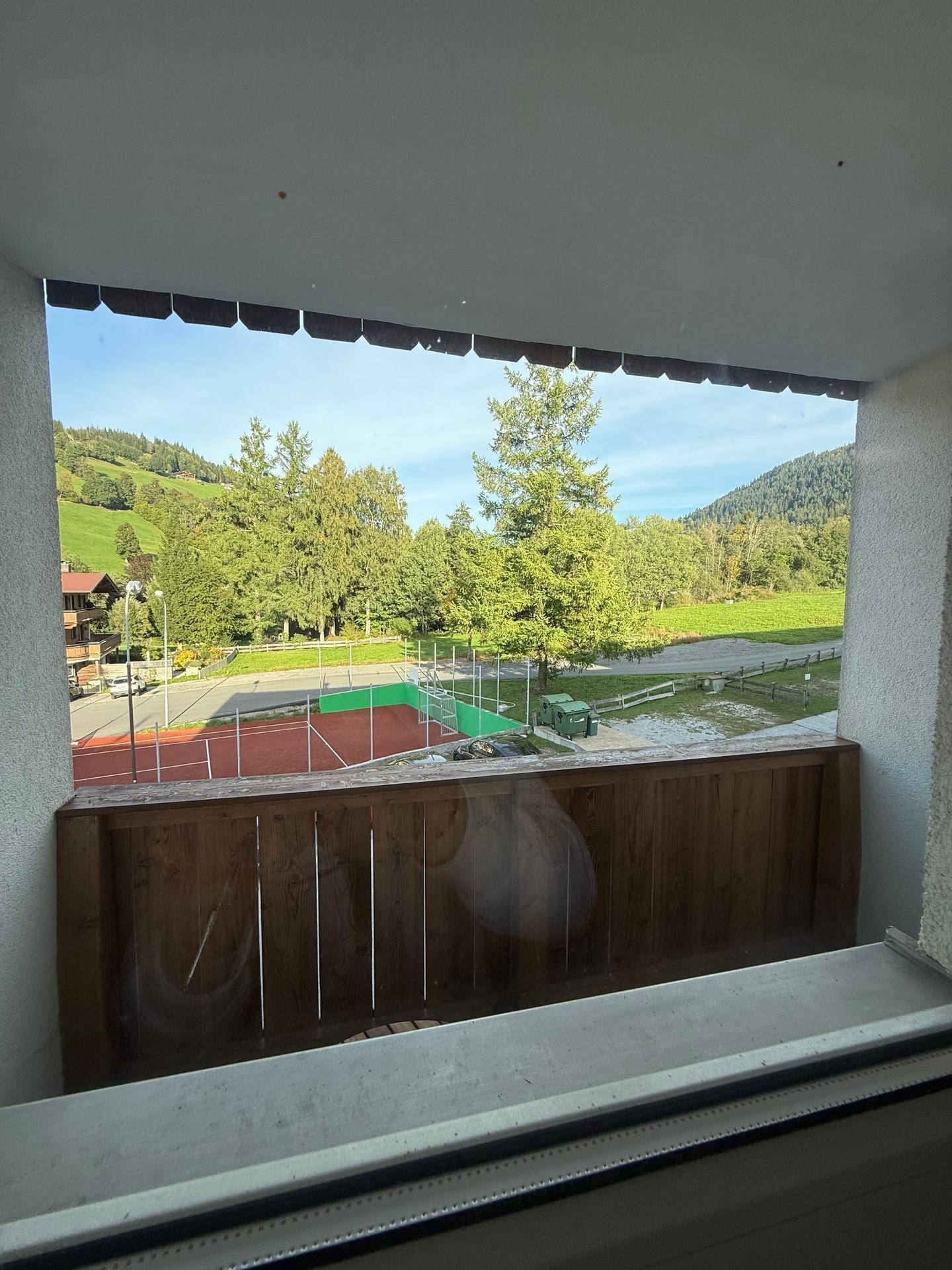 Balkon mit Blick auf Tennisplatz und grüne Hügellandschaft.