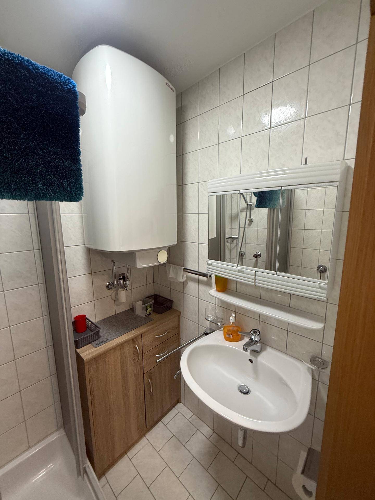Badezimmer mit Waschbecken, Spiegelschrank und Warmwasserboiler über dem Waschtisch.