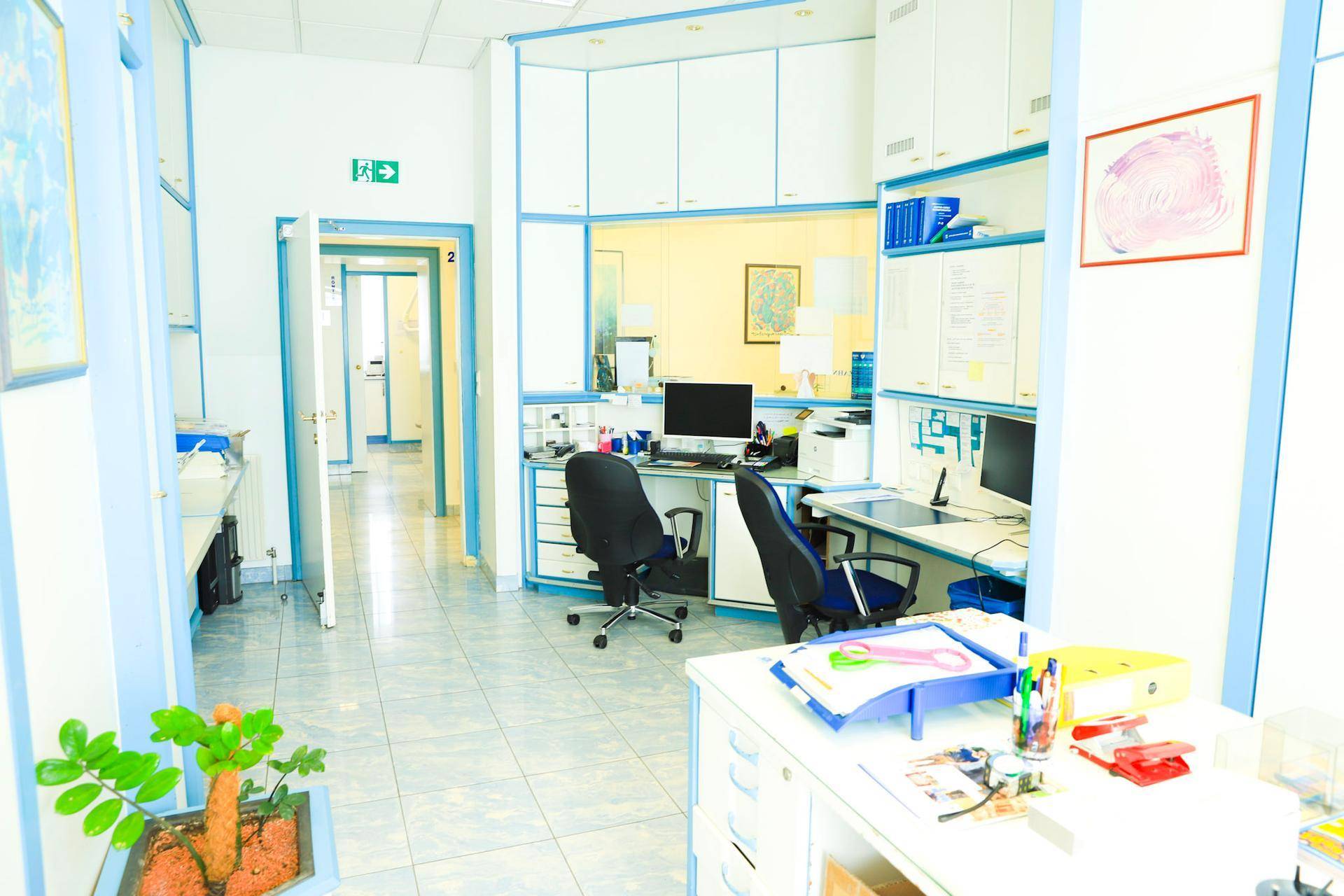 Empfangsbereich oder Büro mit mehreren Arbeitsplätzen, blauen Akzenten und weißen Schränken.