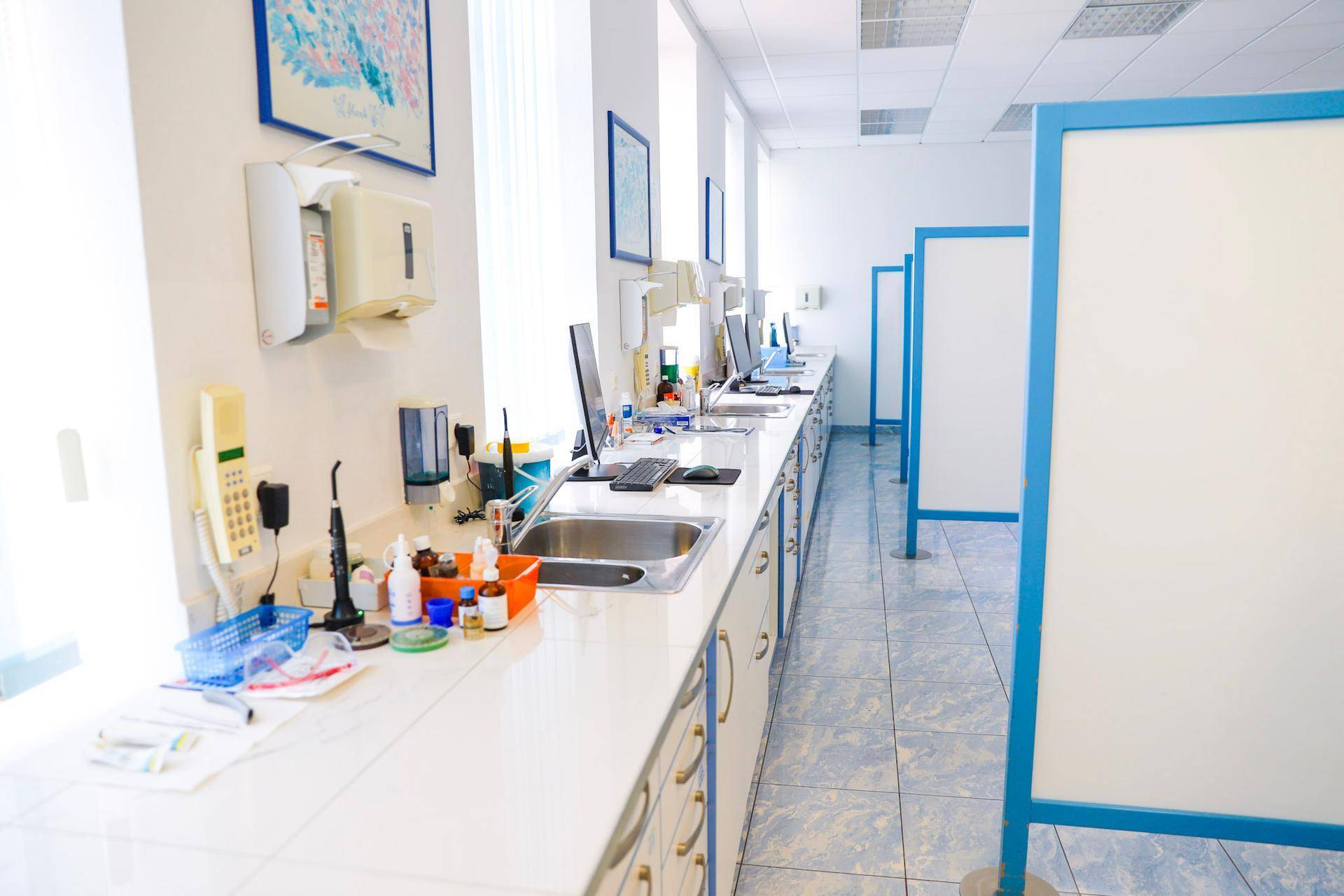 Langer Arbeitsbereich mit Waschbecken, Computern und medizinischen Utensilien entlang der Wand.