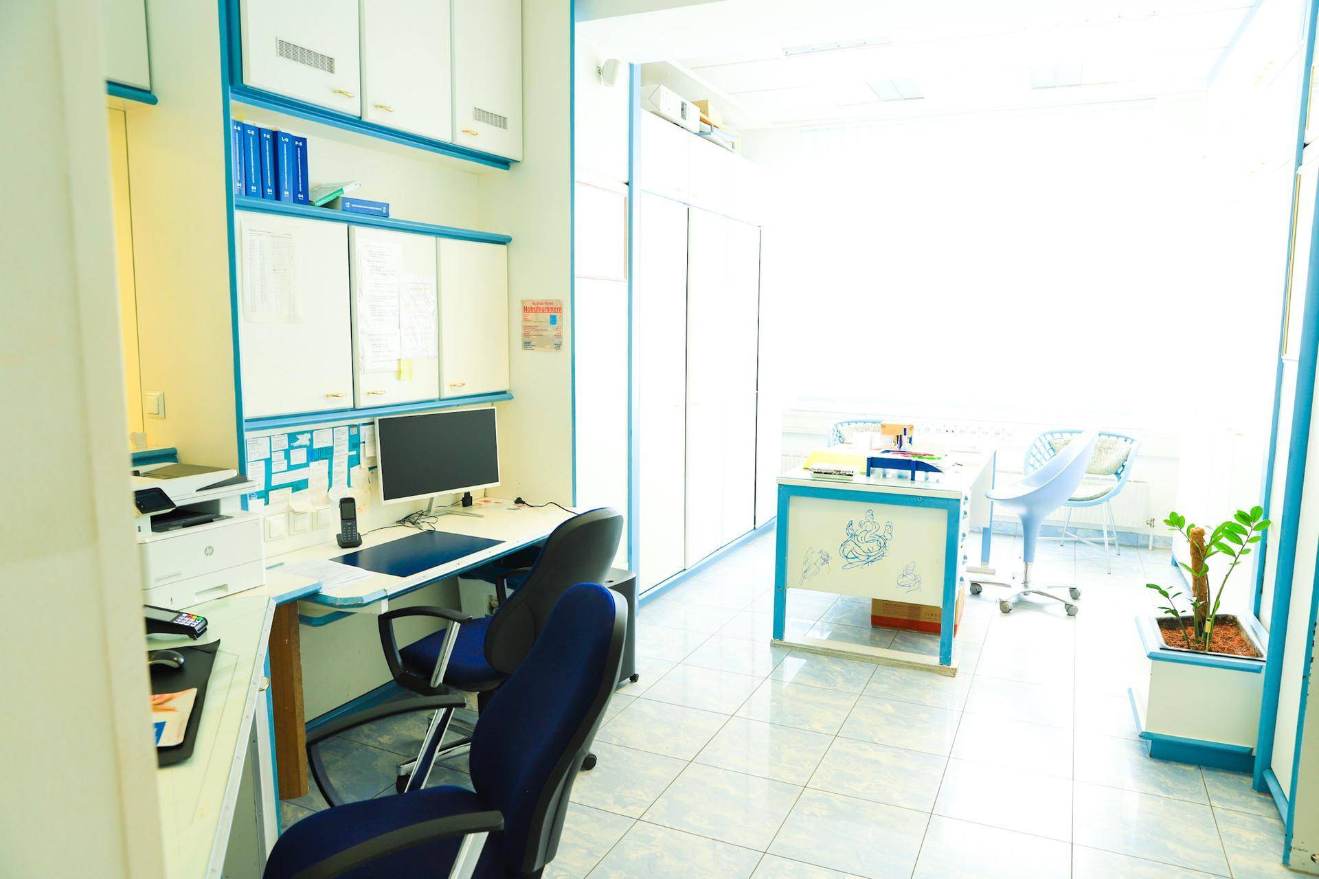 Helles Büro mit Schreibtischen, Bürostühlen und weißen Schränken, durchflutet von natürlichem Licht.